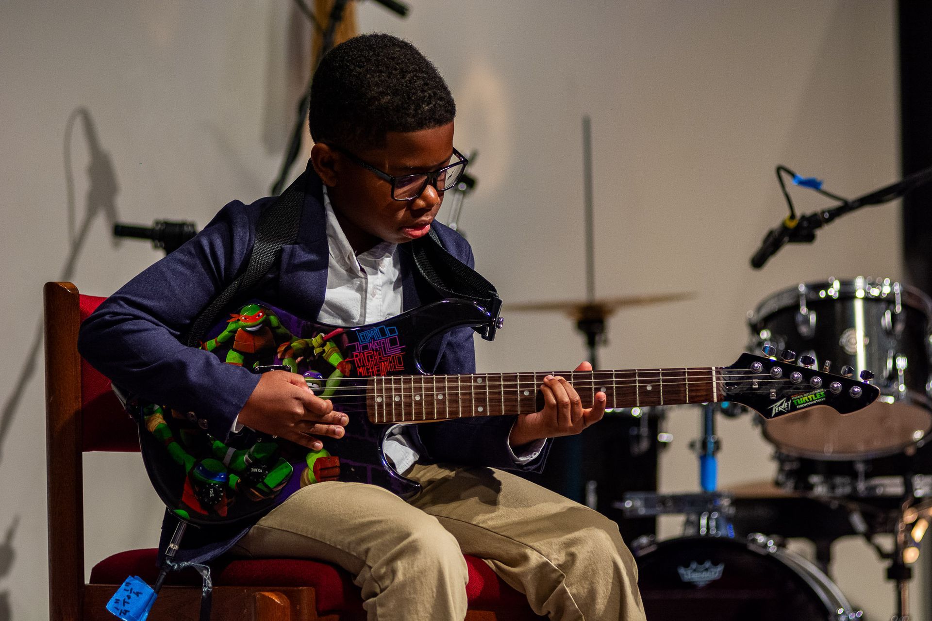 A young boy is sitting in a chair playing a guitar.
