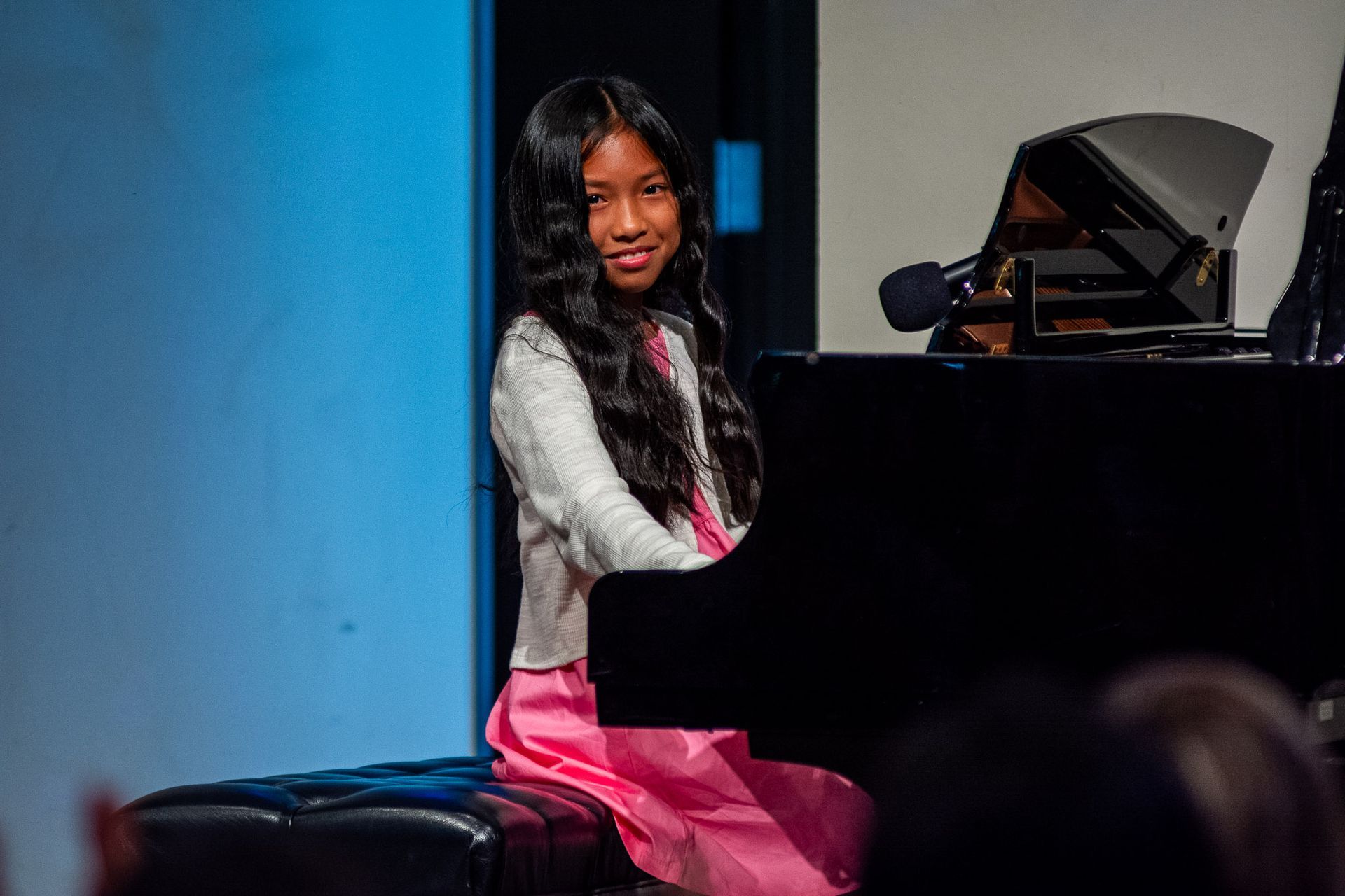 A young girl is sitting at a piano with a microphone in front of her.