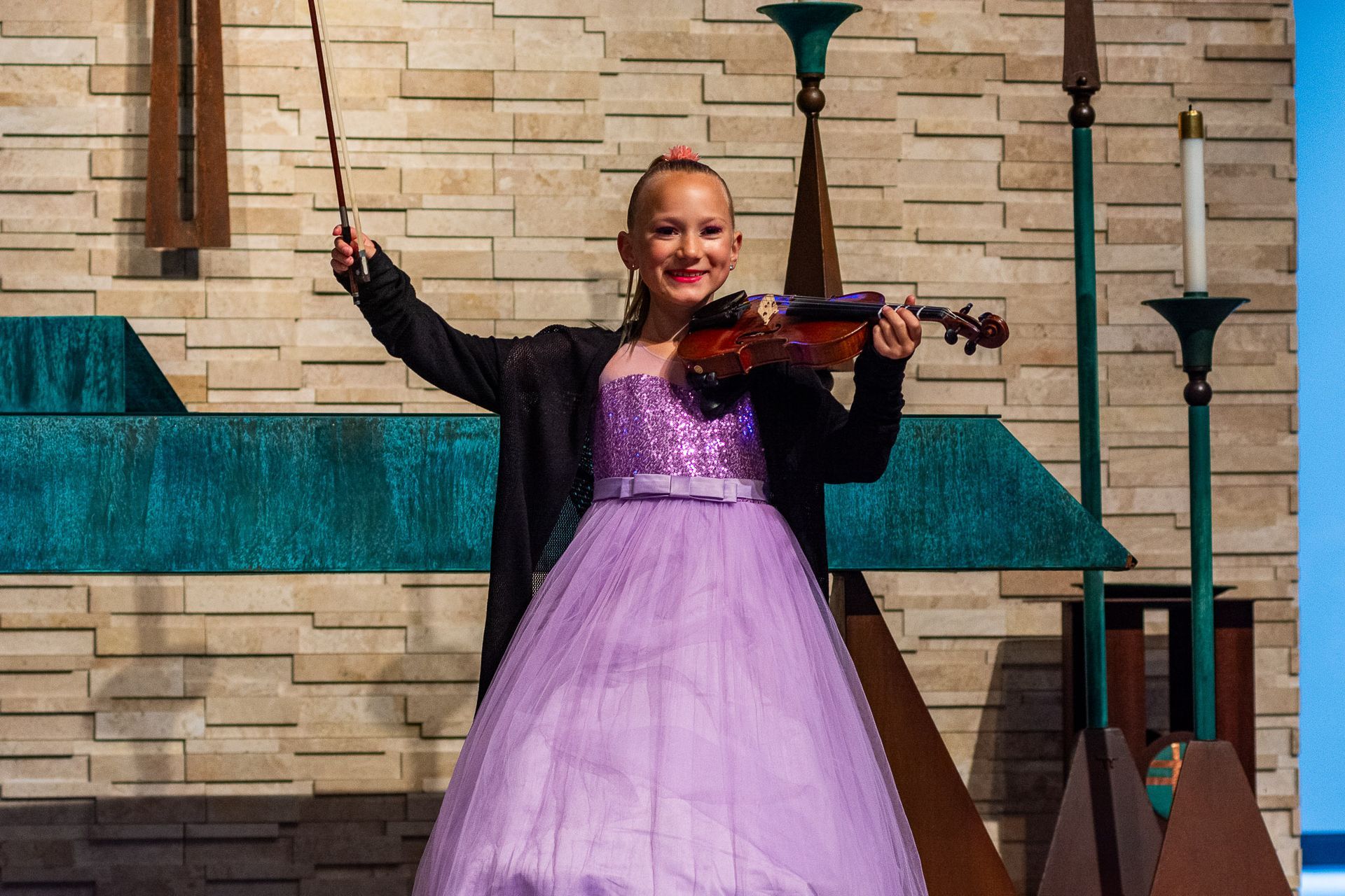 A young girl in a purple dress is playing a violin.