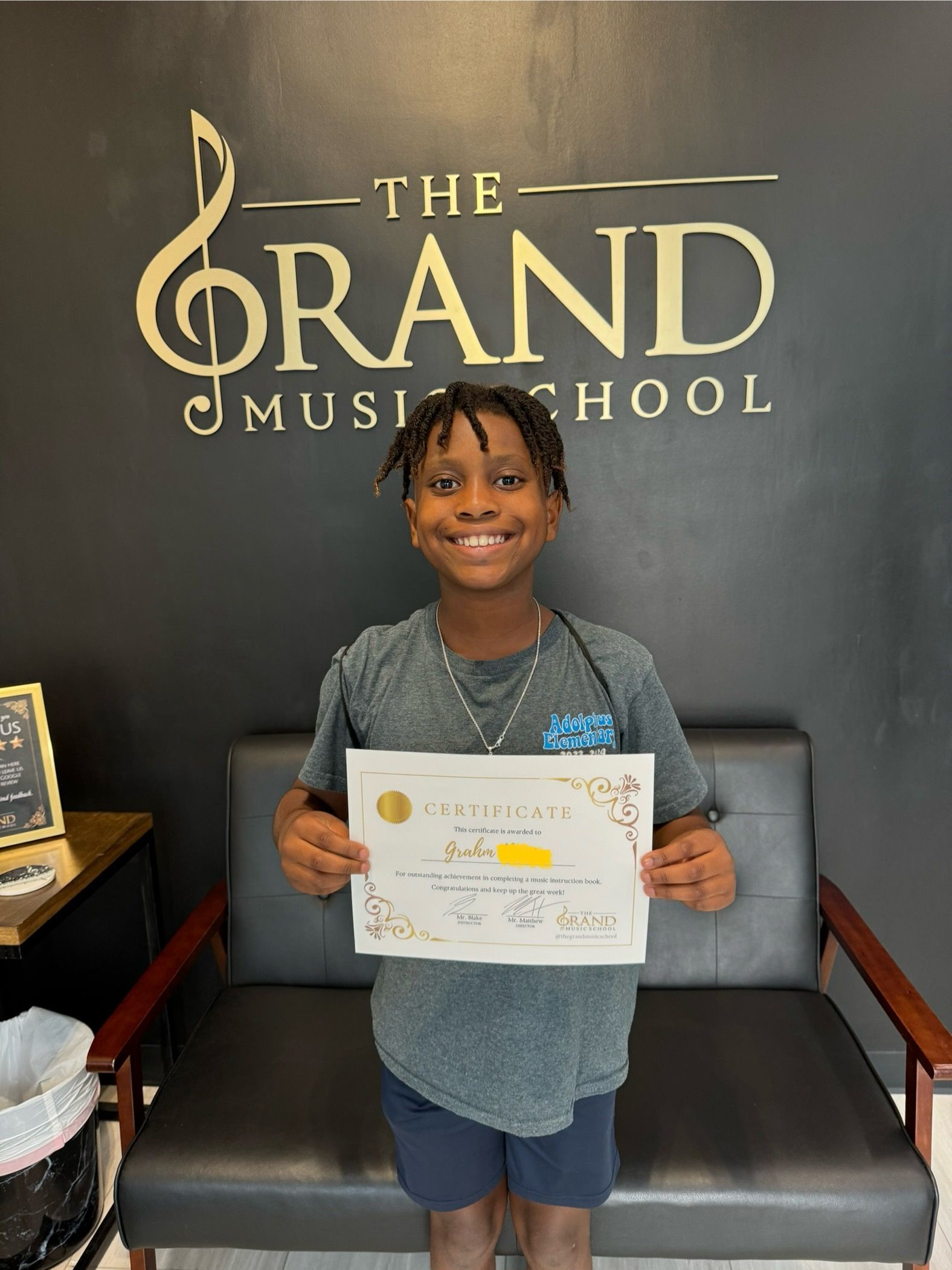 A young boy is holding a certificate in front of the grand music school