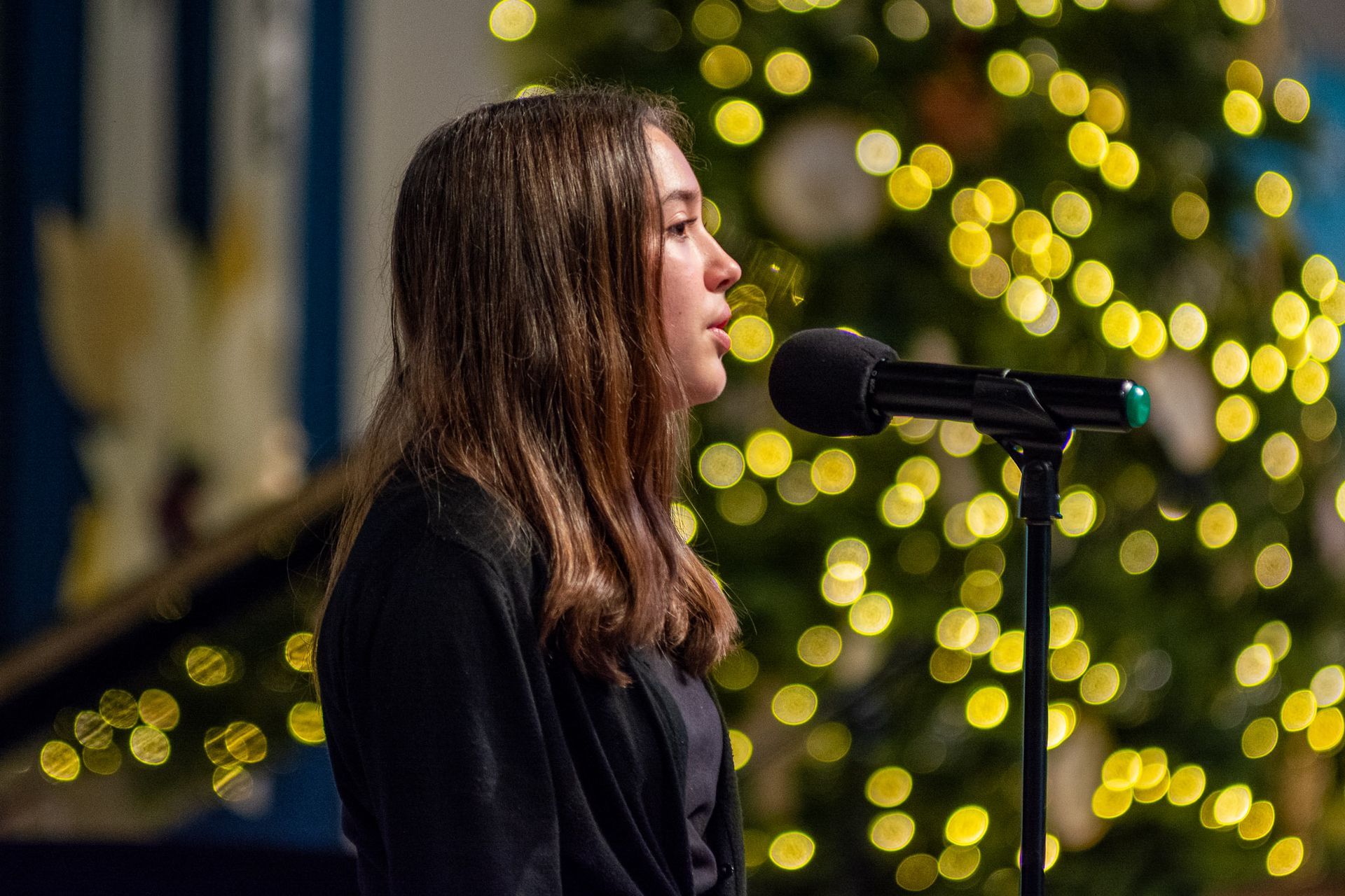 A woman is singing into a microphone in front of a christmas tree.