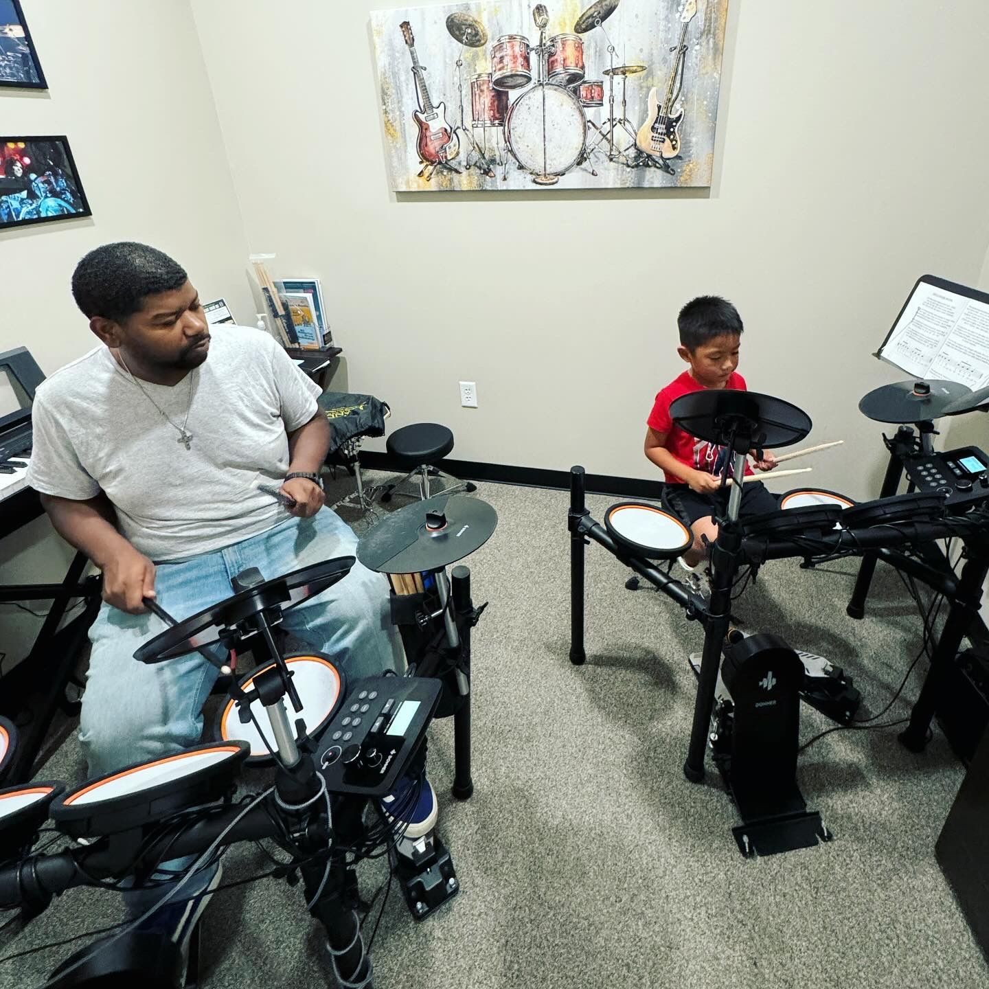 A man and a boy are playing electronic drums in a room.
