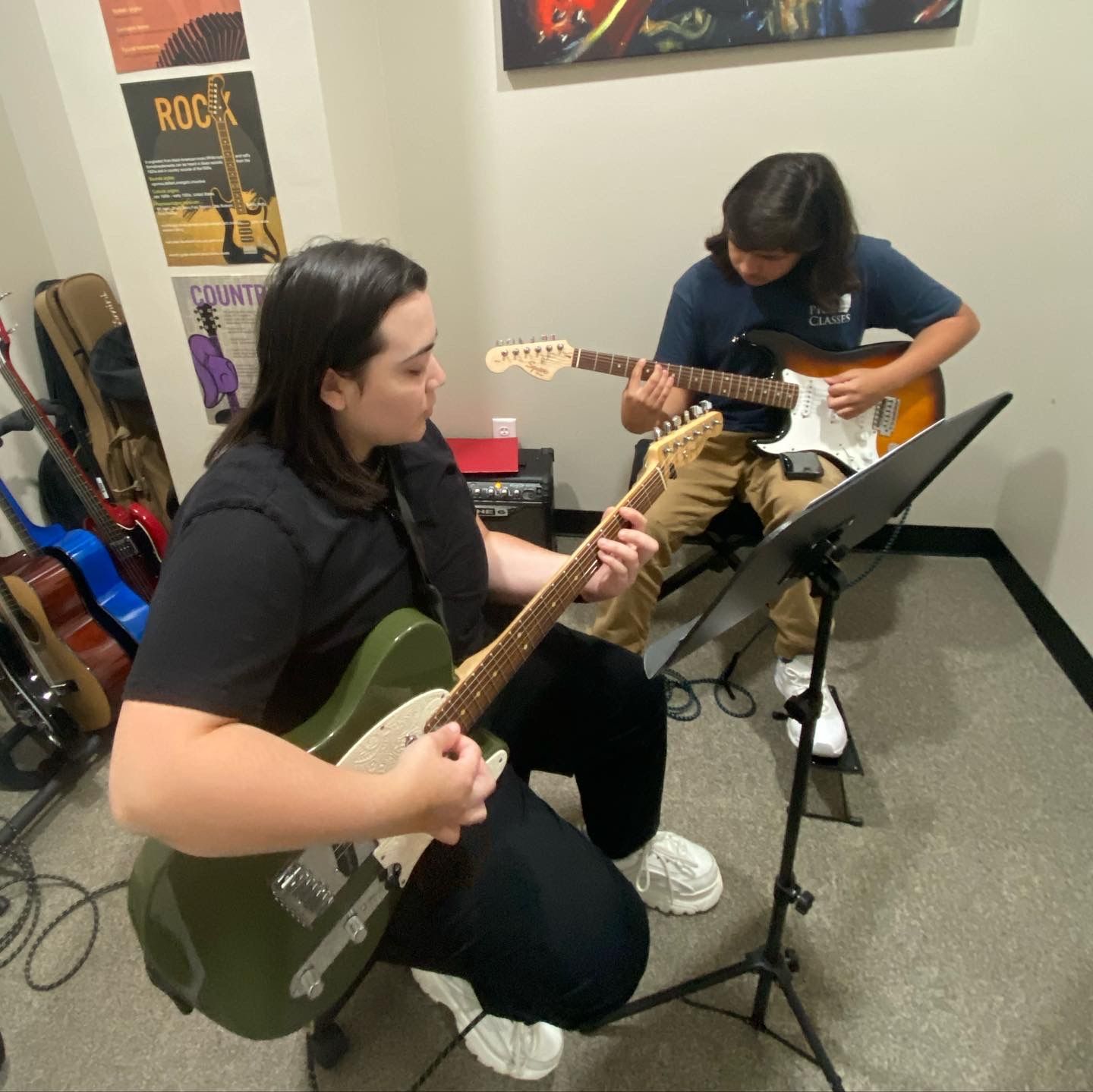 Two people playing guitars in a room with a poster on the wall that says rock