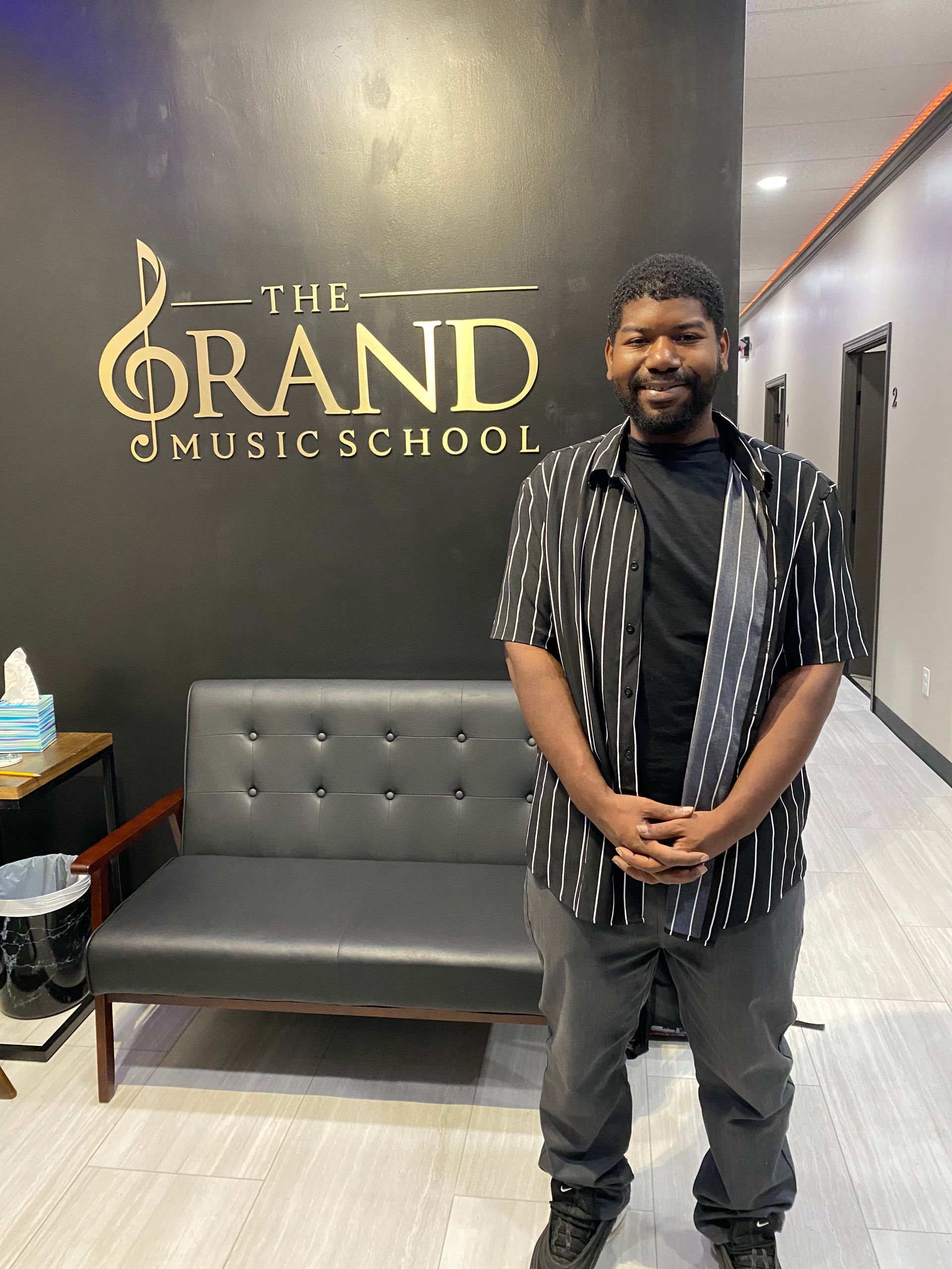 A man is standing in front of a wall that says the grand music school.