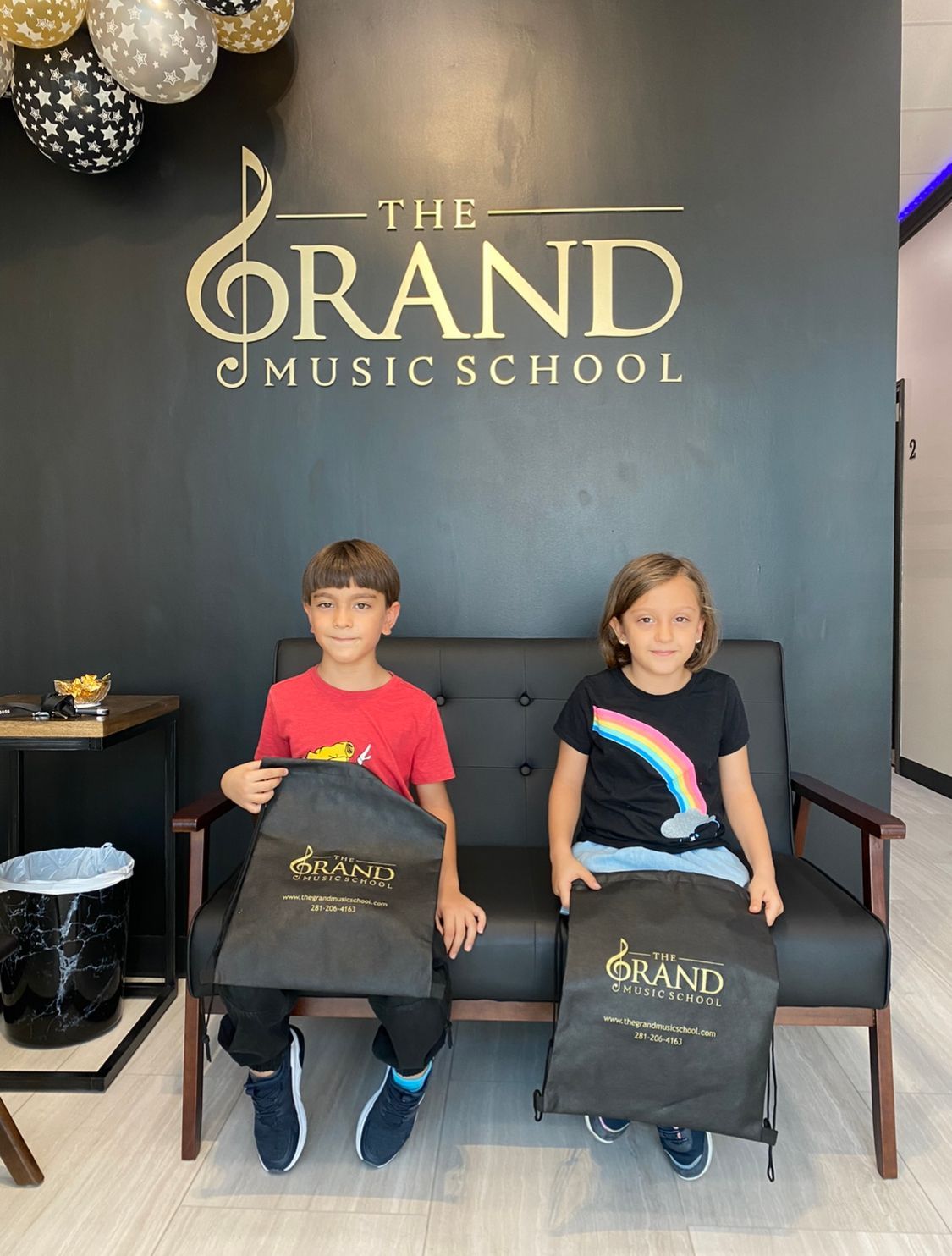 A boy and a girl are sitting on a couch in front of a sign for the grand music school.
