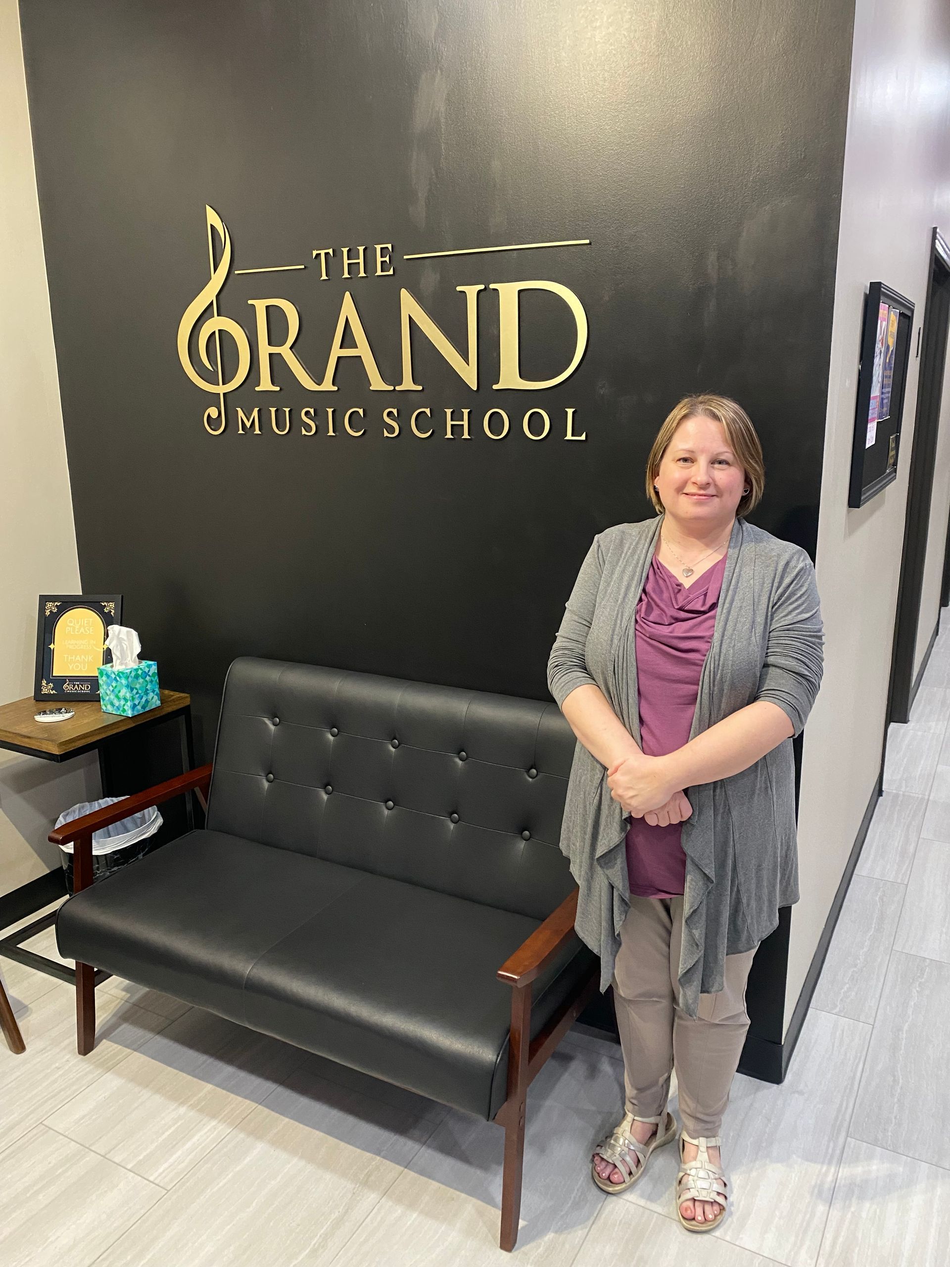 A woman is standing in front of a couch in a waiting room at the grand music school.