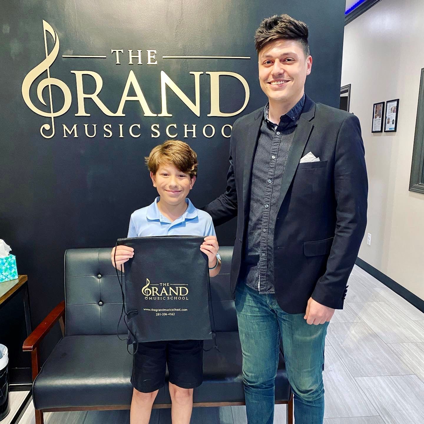 A man and a boy are standing in front of a sign that says the grand music school.