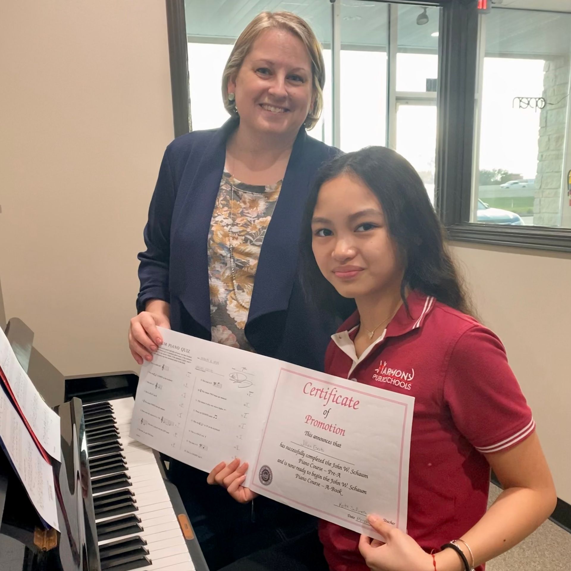 A woman and a girl are holding a certificate in front of a piano.