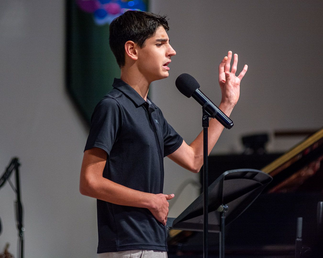 A young man is singing into a microphone on a stage.