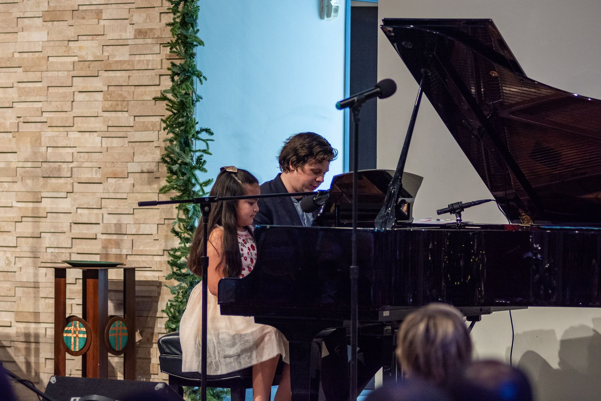 A man and a girl are playing a piano in front of a crowd.