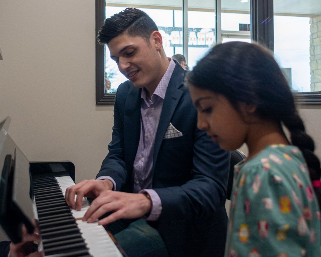 A man is teaching a young girl how to play the piano.