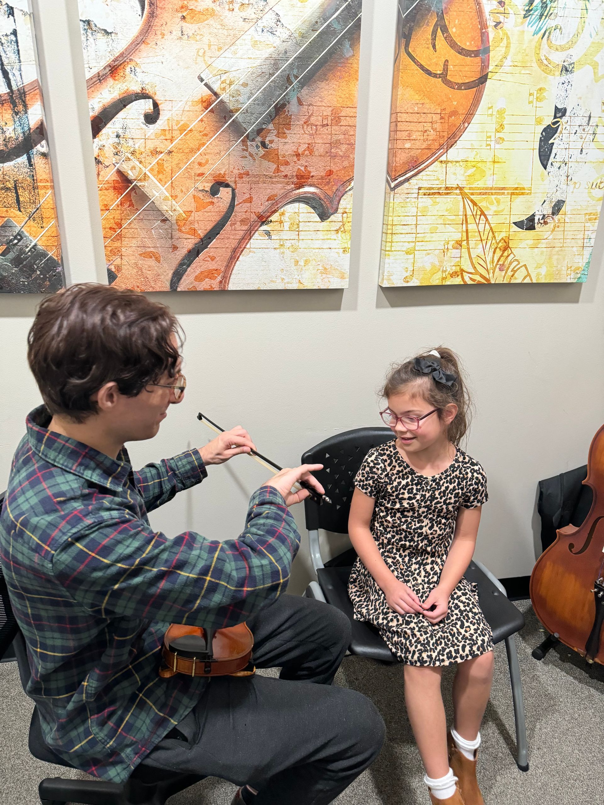 A man is teaching a little girl how to play a violin.
