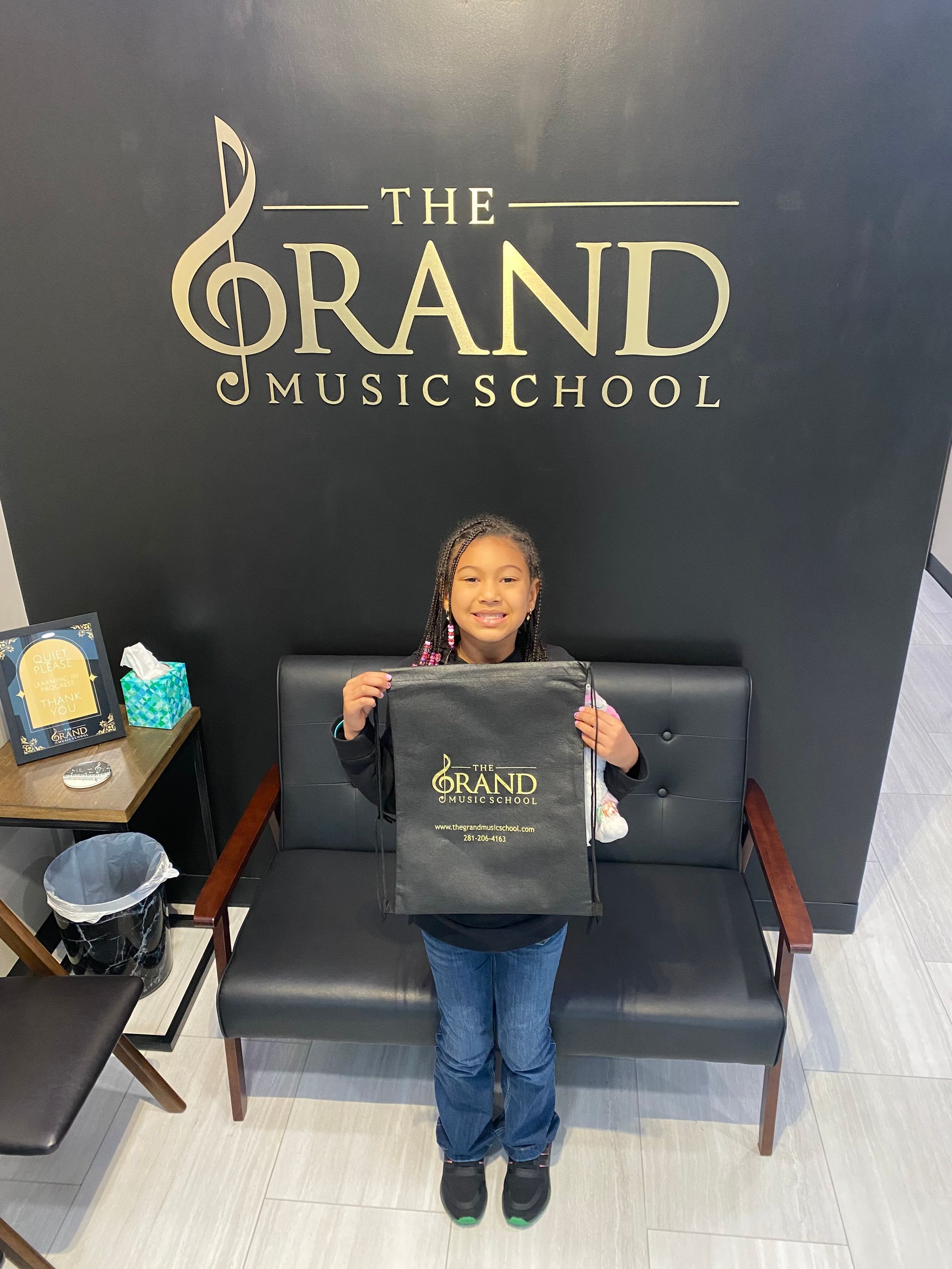 A little girl is standing in front of a couch holding a bag.