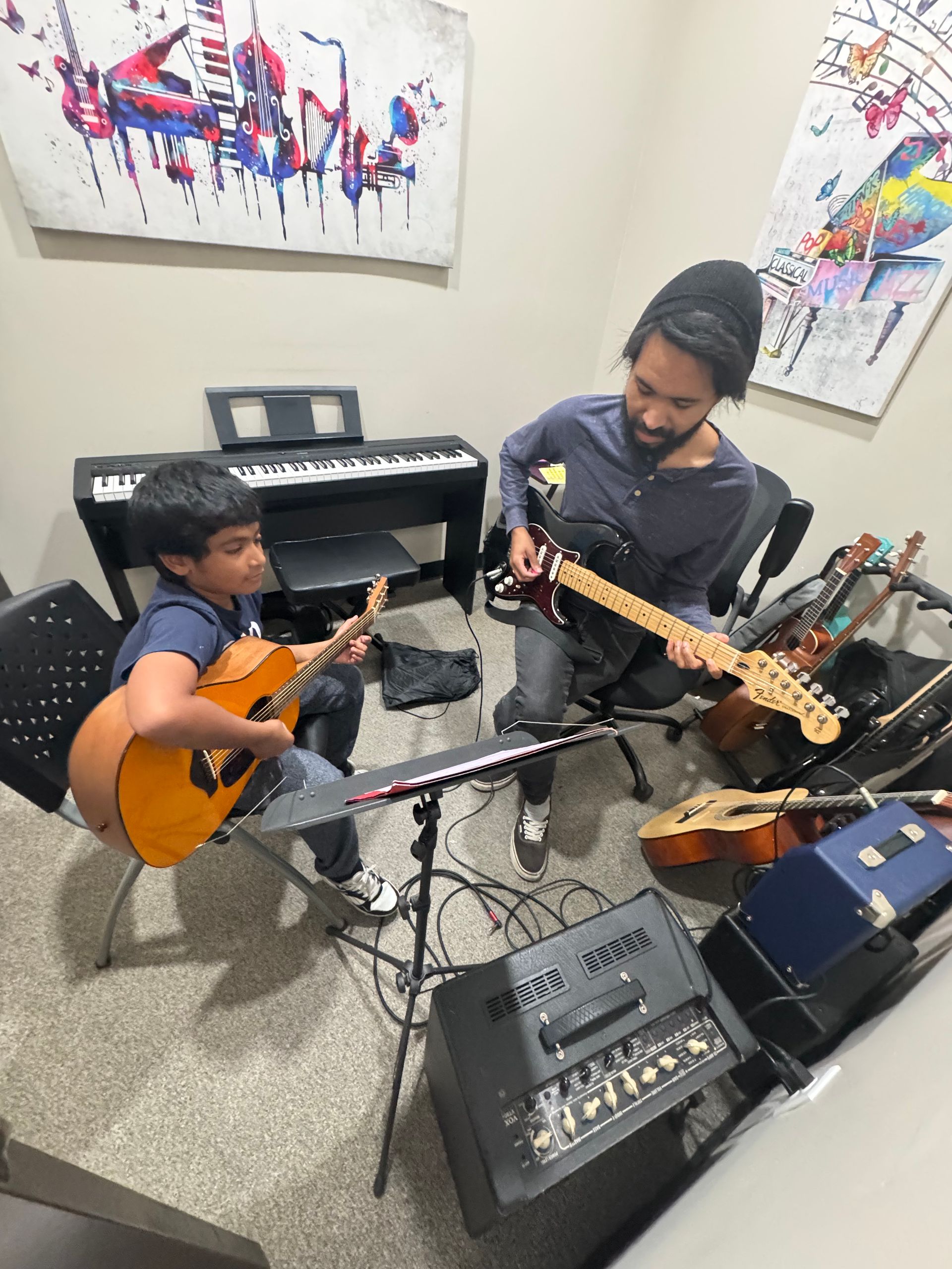 A man and a boy are playing guitars in a room.