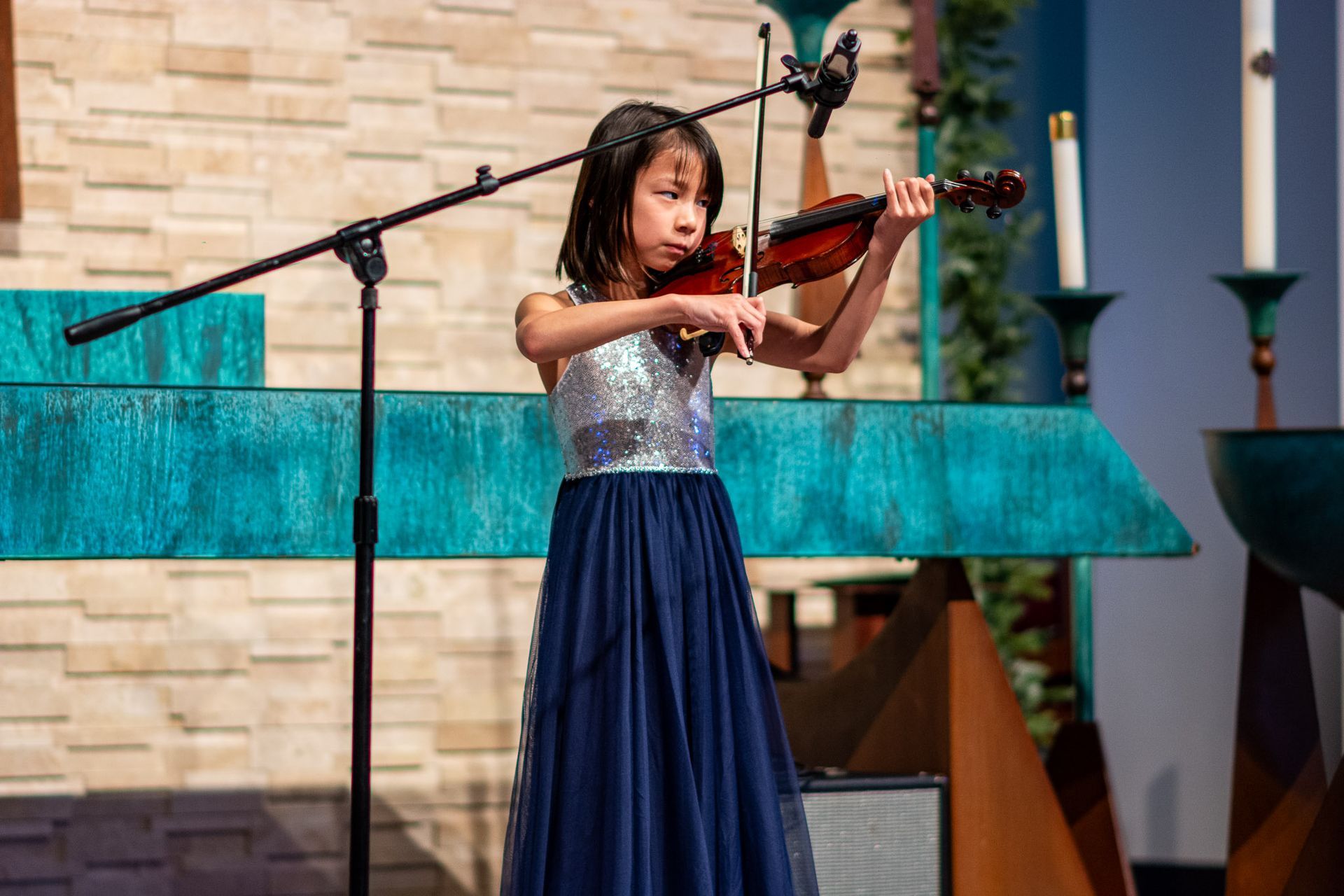 A young girl is playing a violin in front of a microphone in a church.