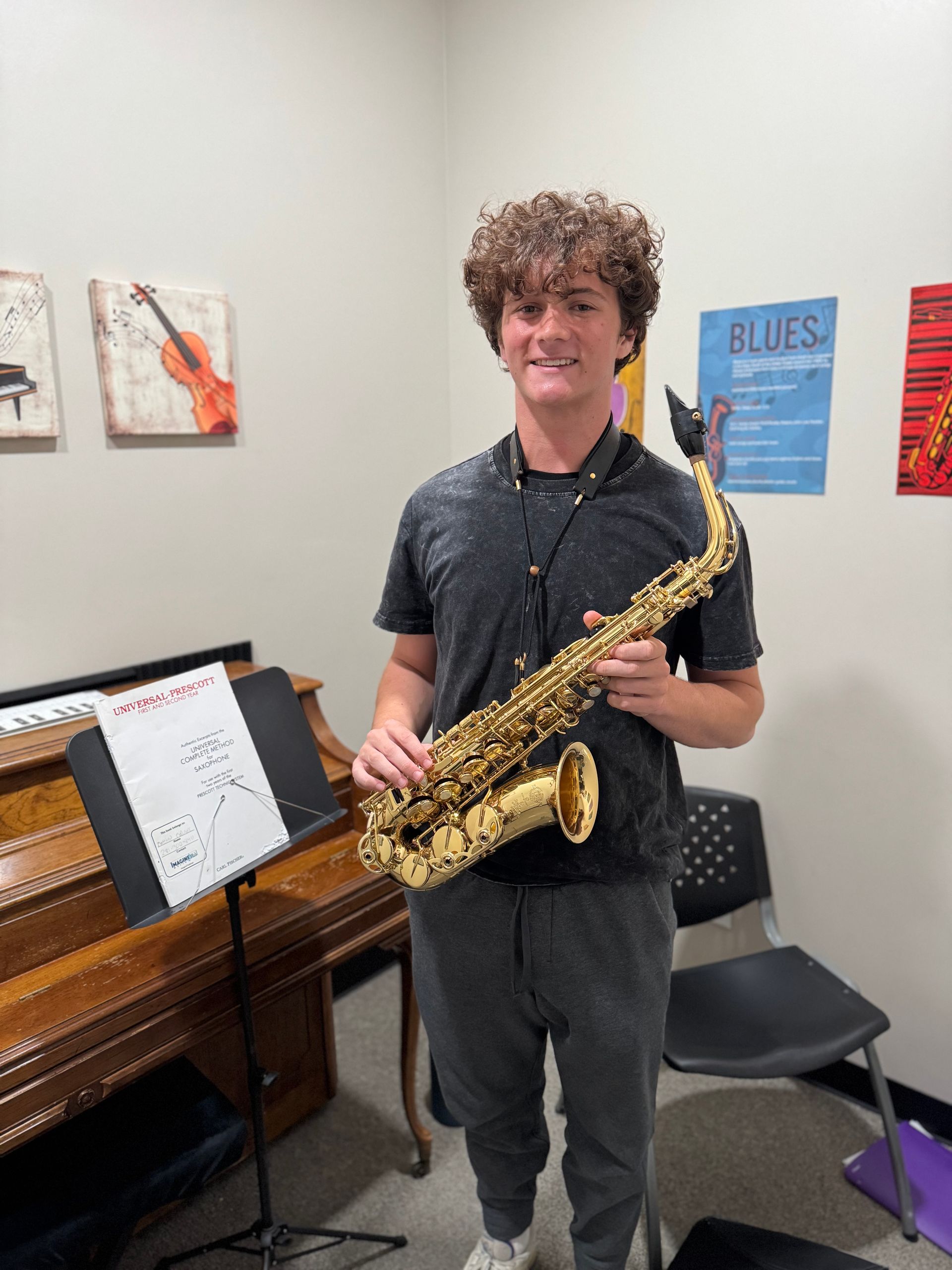 A young man is holding a saxophone in a music room.