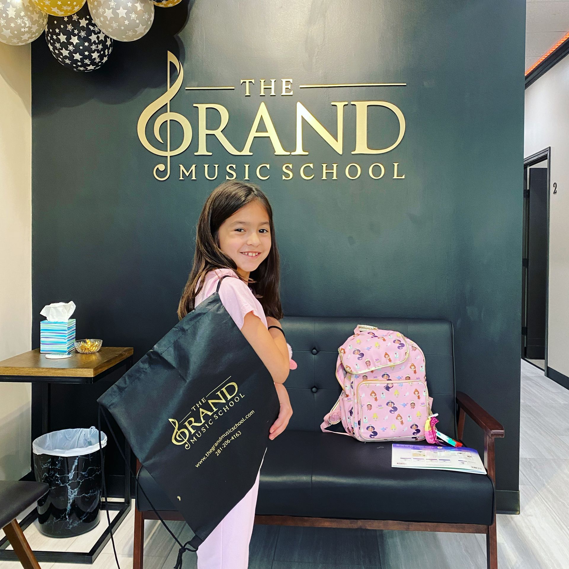 A little girl is standing in front of a wall that says the grand music school