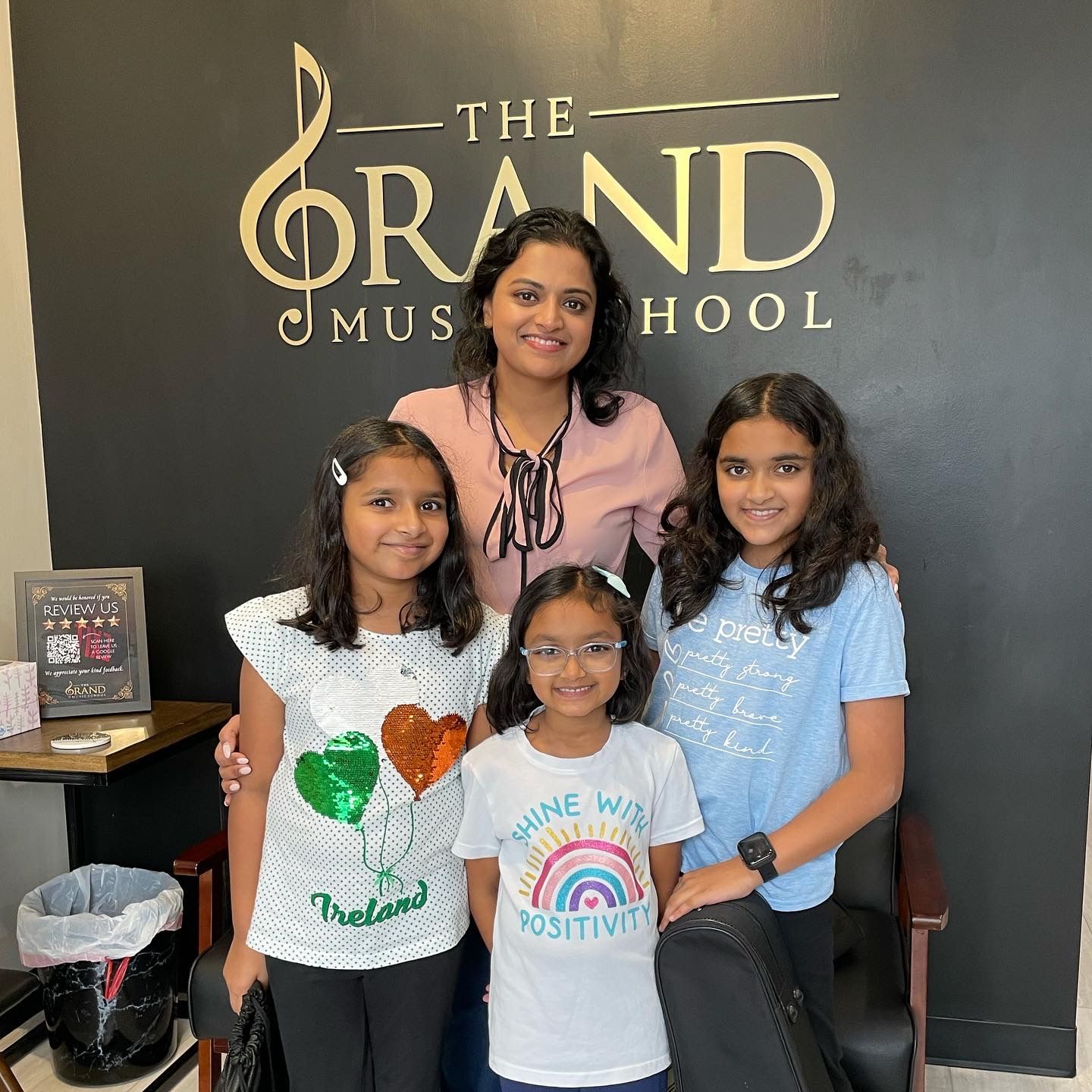 A woman and three girls are posing for a picture in front of a sign that says the grand music school