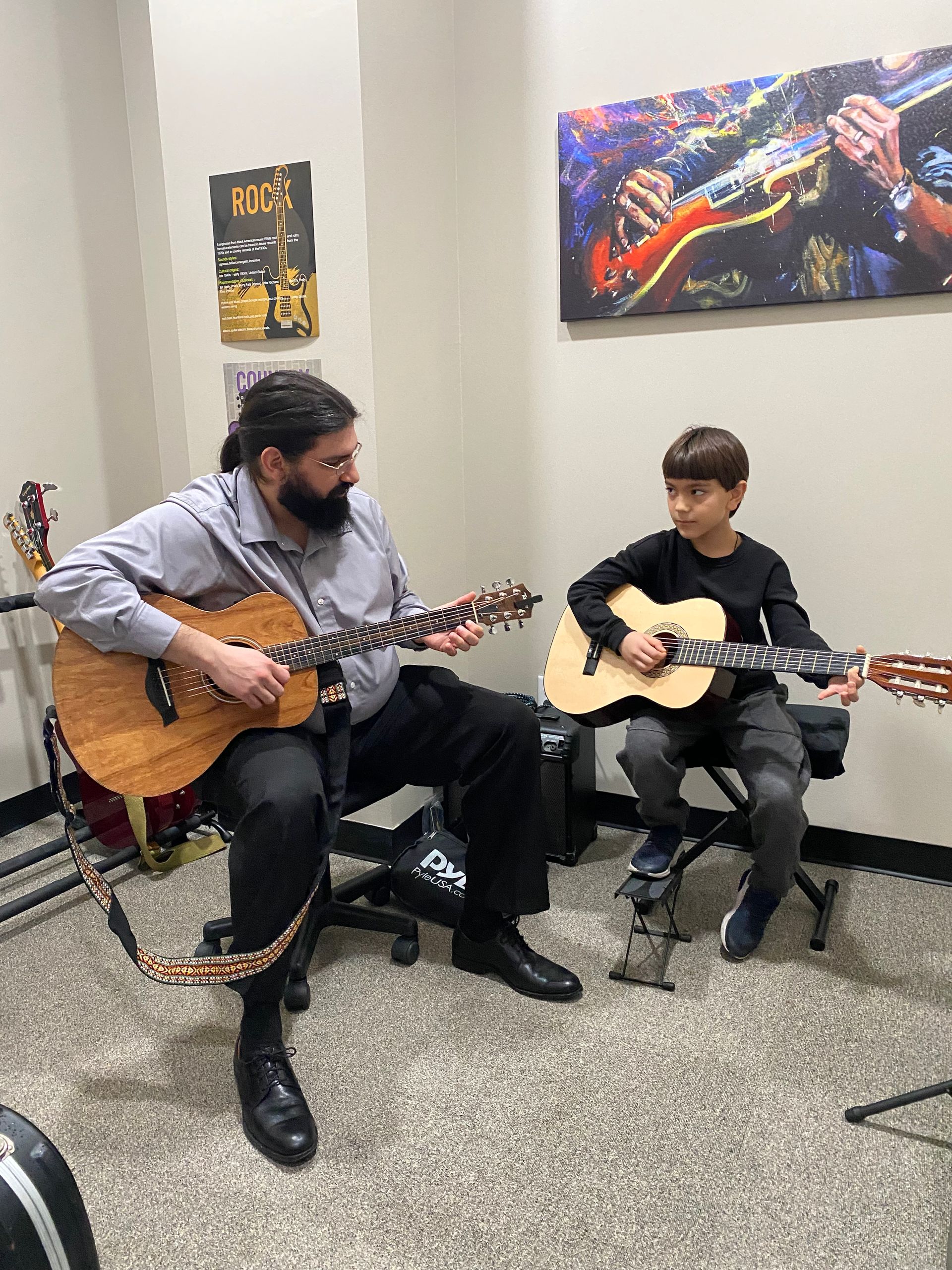 A man and a boy are playing guitars in a room.