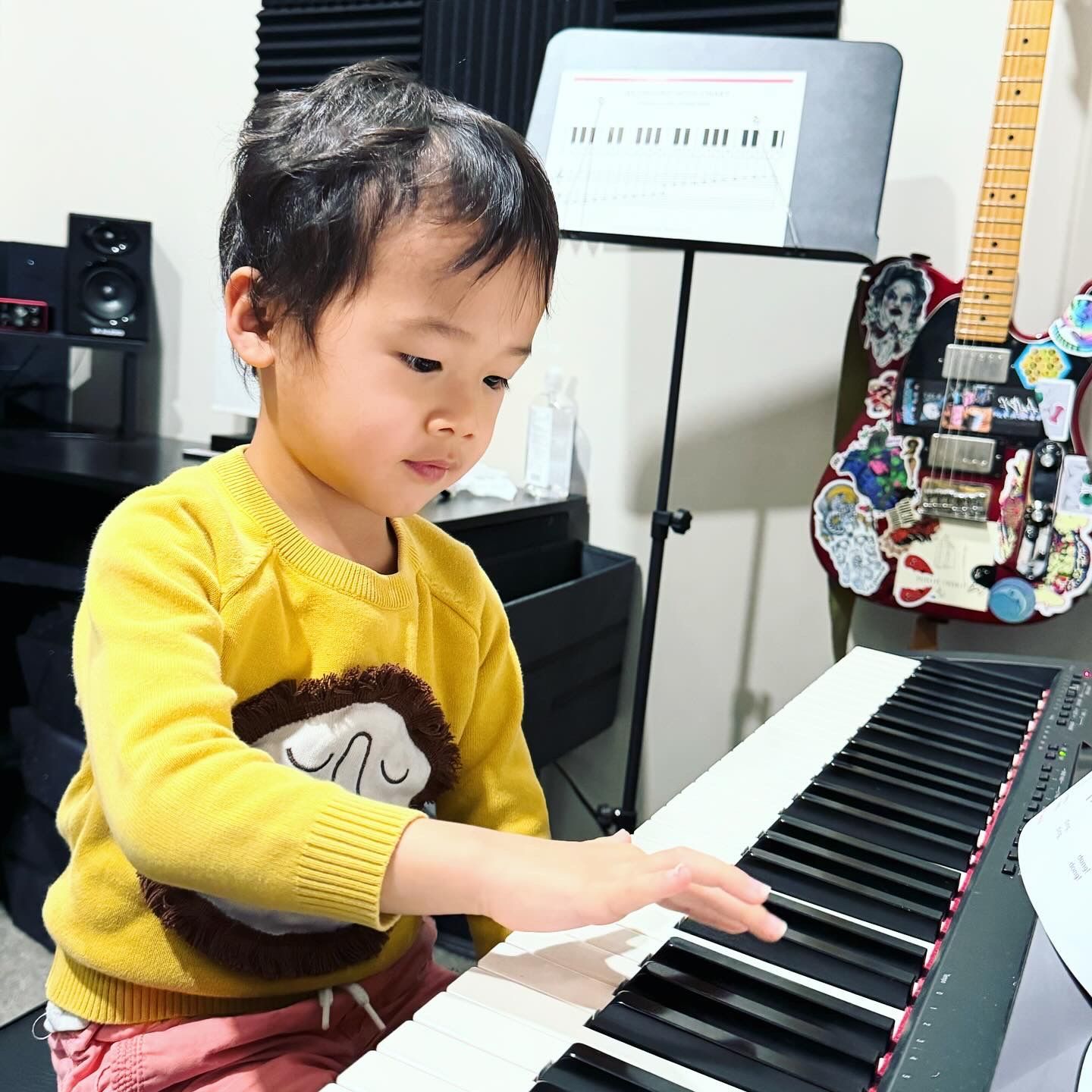 A little boy in a yellow sweater is playing a piano