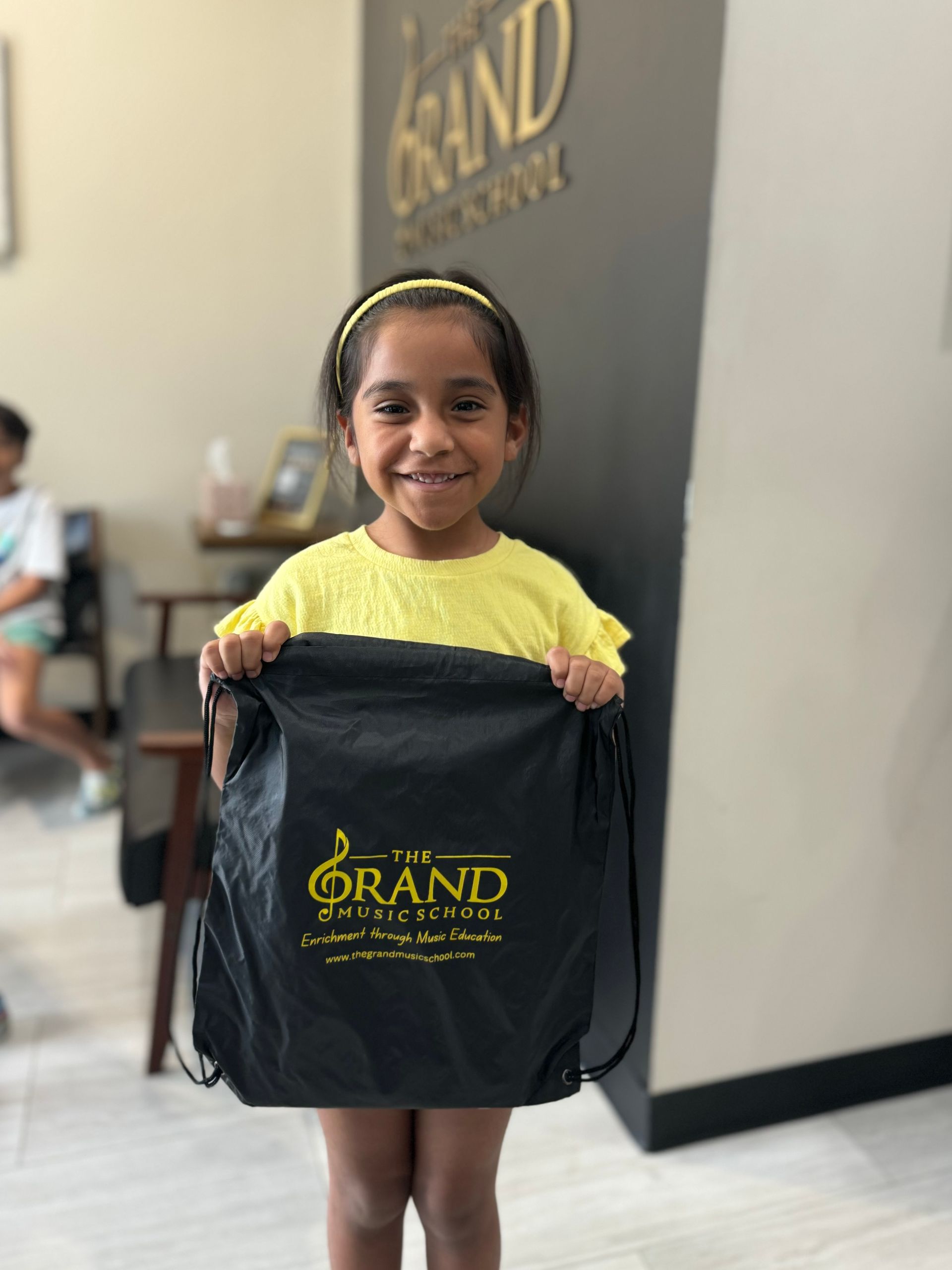 A little girl is holding a black bag that says grand on it