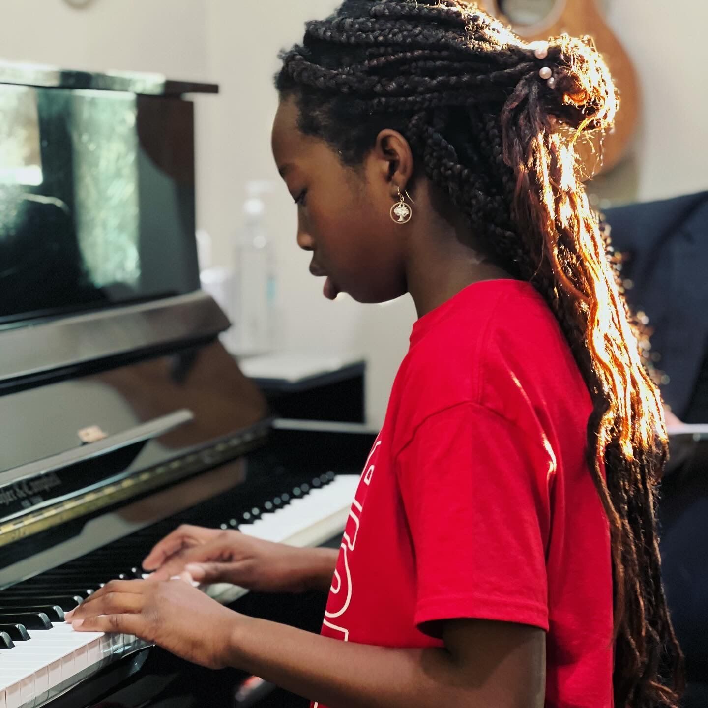 A girl in a red shirt is playing a piano