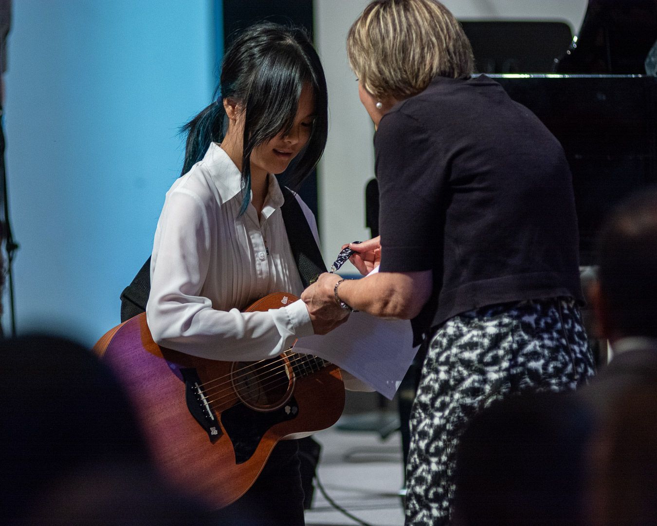 A woman is shaking hands with a girl holding a guitar.