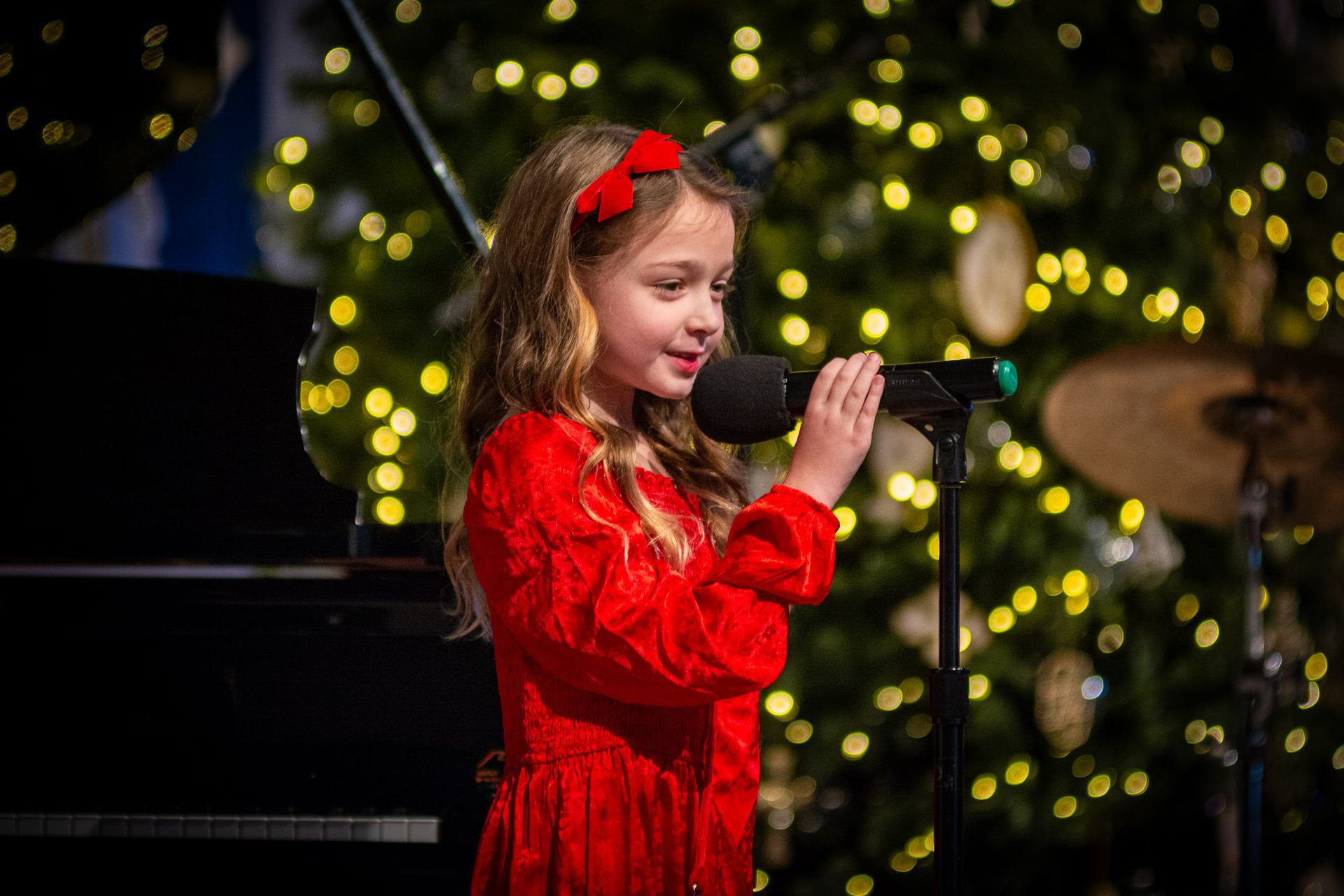 A little girl in a red dress is singing into a microphone.