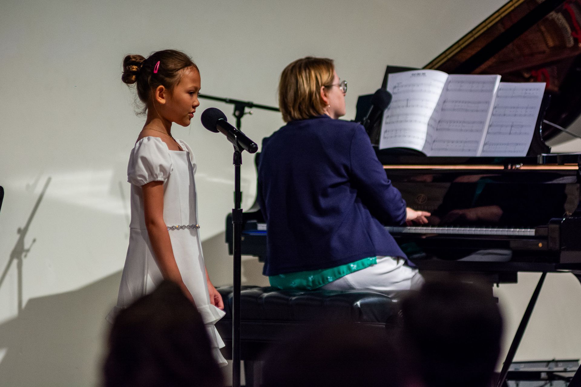 A woman is playing a piano and a girl is singing into a microphone.