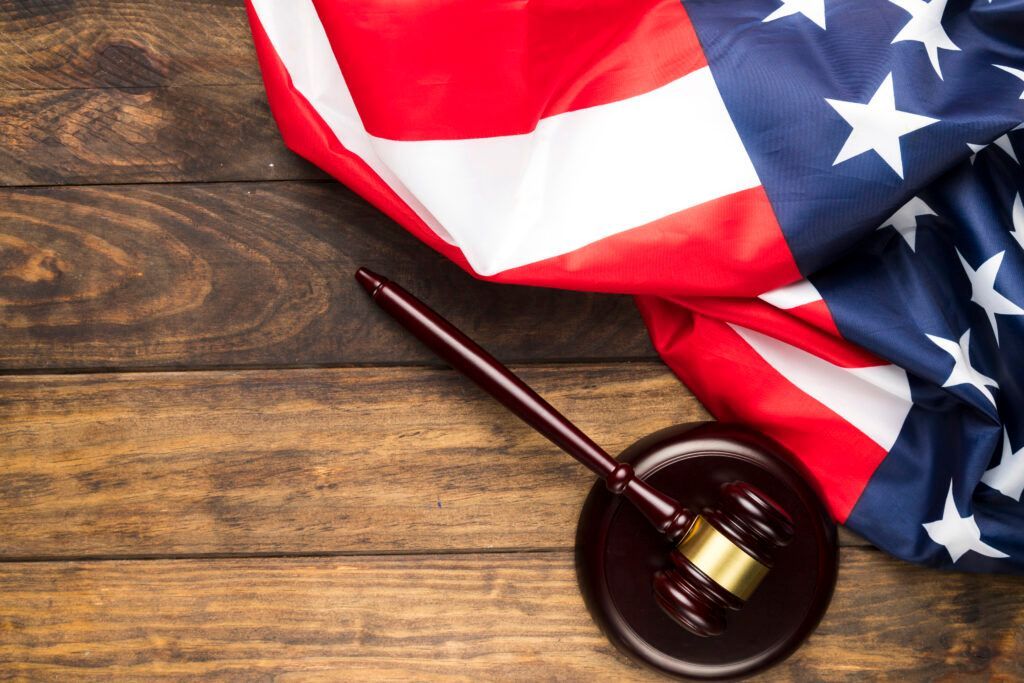 An american flag and a judge 's gavel on a wooden table.