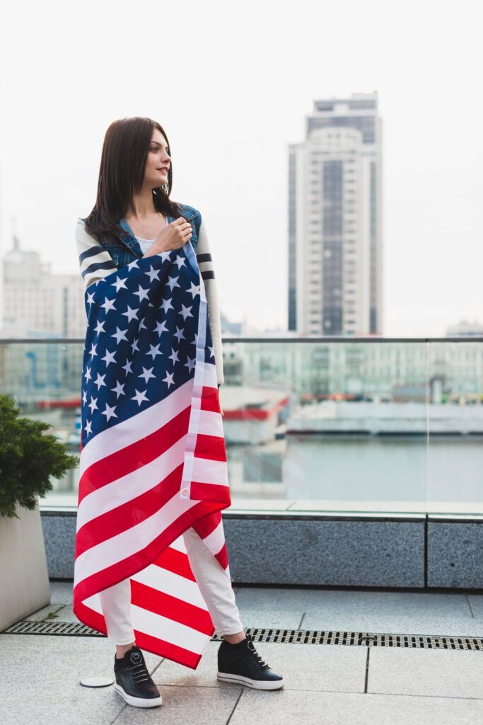 A woman is standing on a balcony holding an american flag.