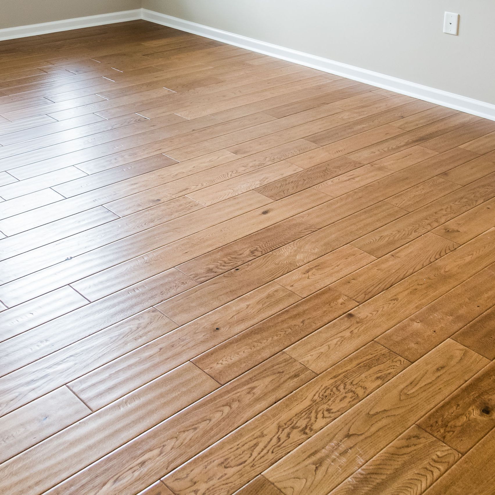 Hardwood floor with a shiny finish, installed in a room with white baseboards and light walls.