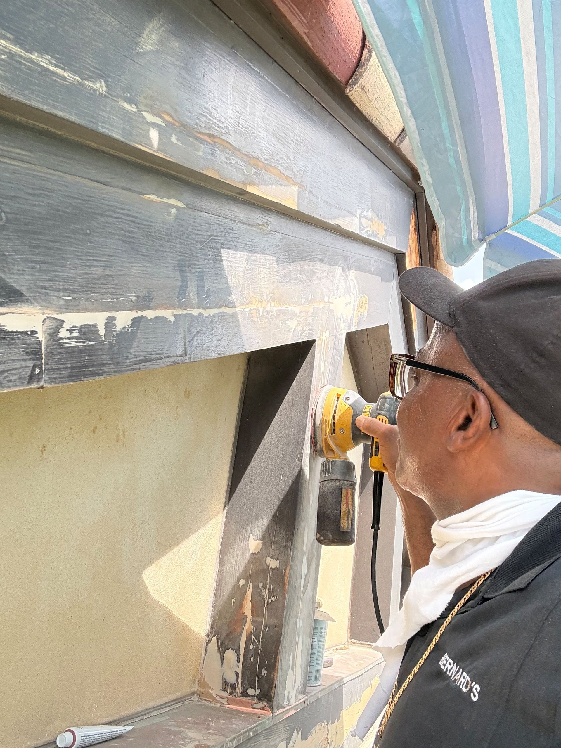 Worker using a power tool on a building exterior under a blue awning