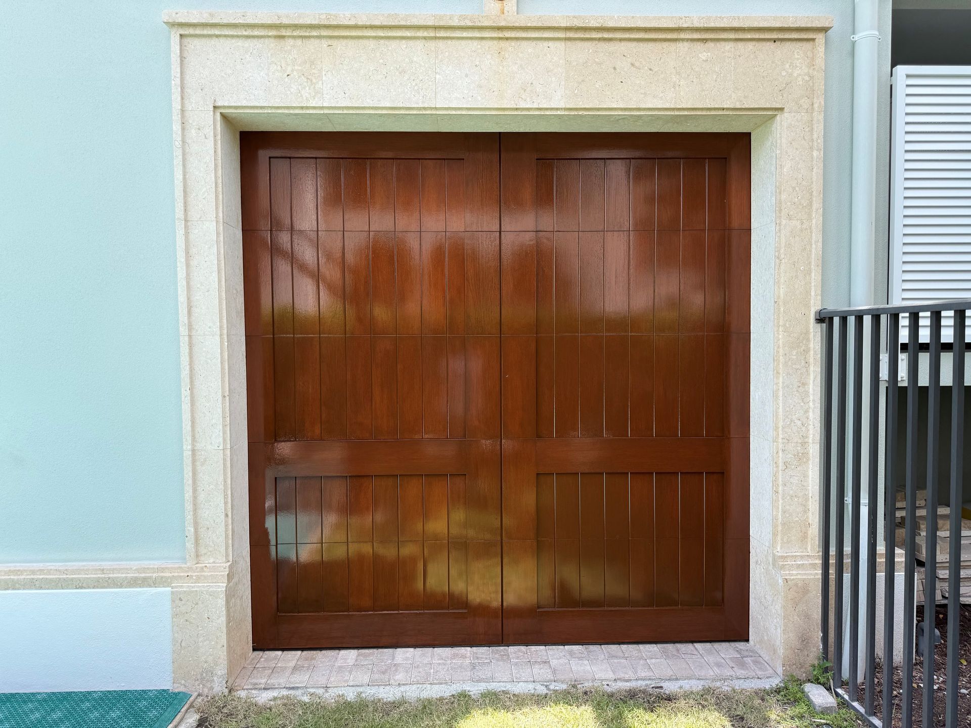 Wooden garage door framed by beige stone in a pale blue exterior wall
