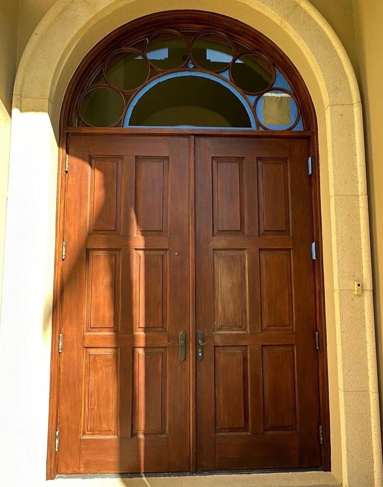 Wooden double entrance door beneath a stone arch with stained-glass windows above