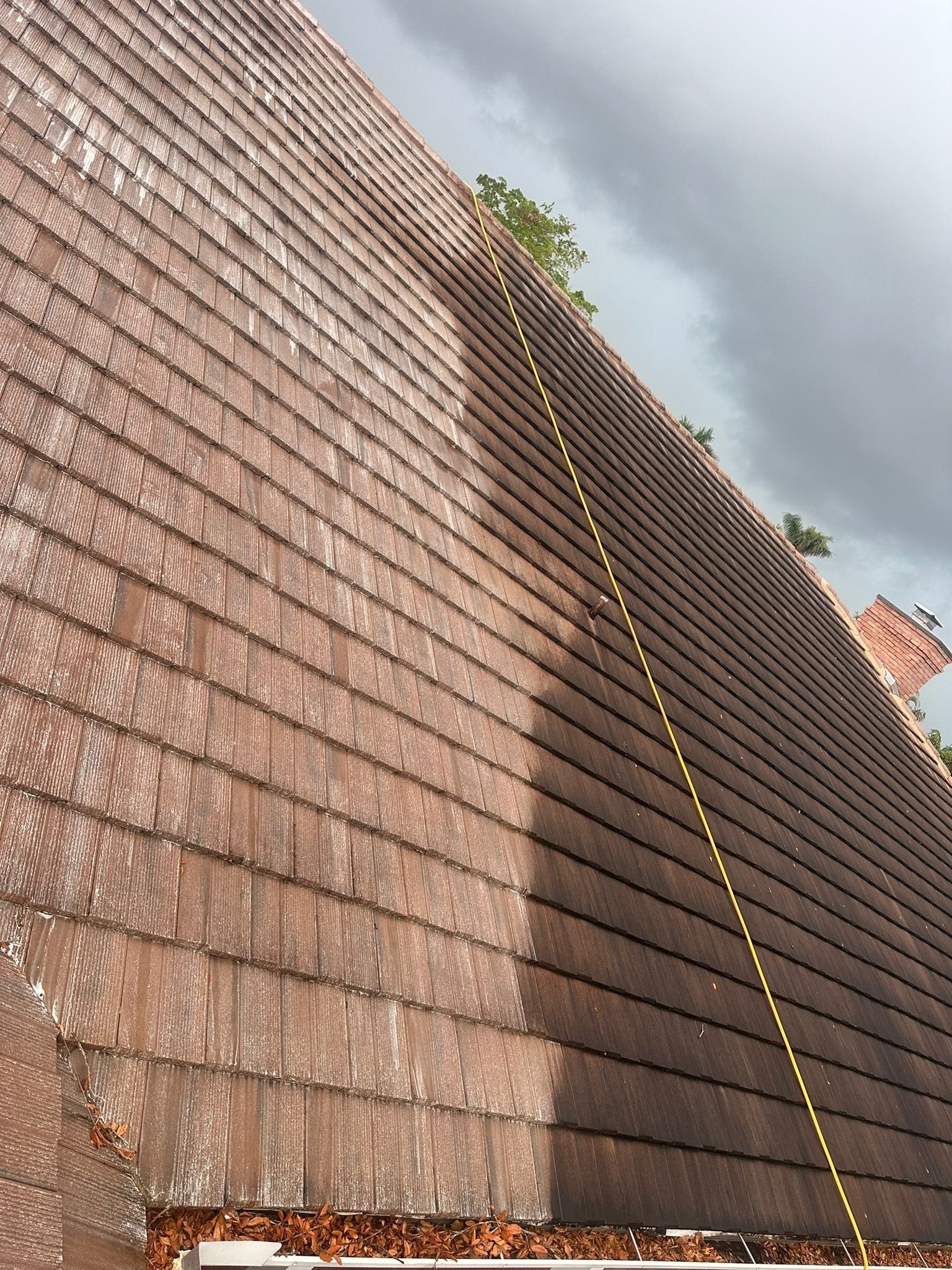 Steep shingled roof with a yellow rope or measuring line running down the slope under a cloudy sky
