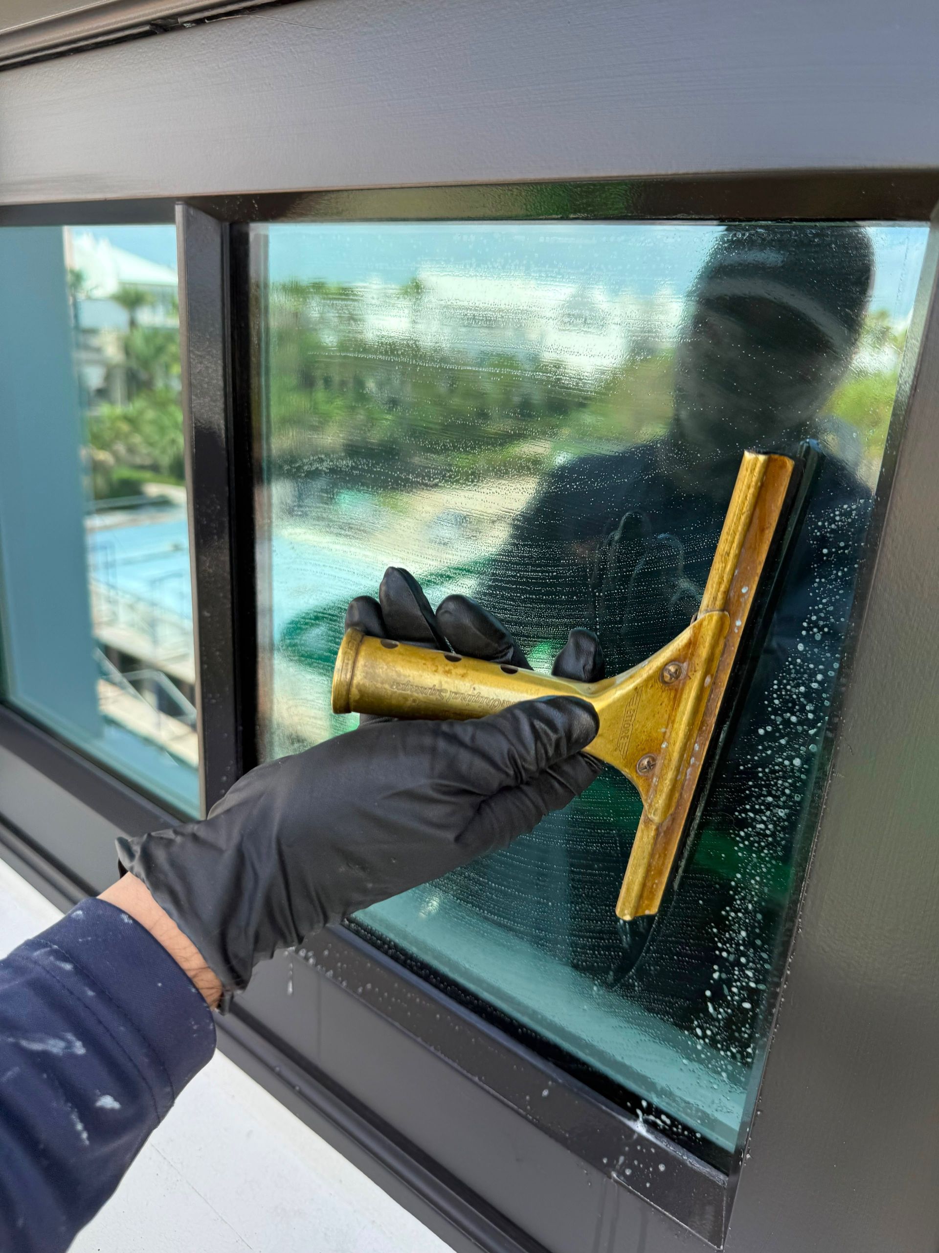 Gloved hand cleaning a rain-speckled window with a yellow squeegee on a building exterior