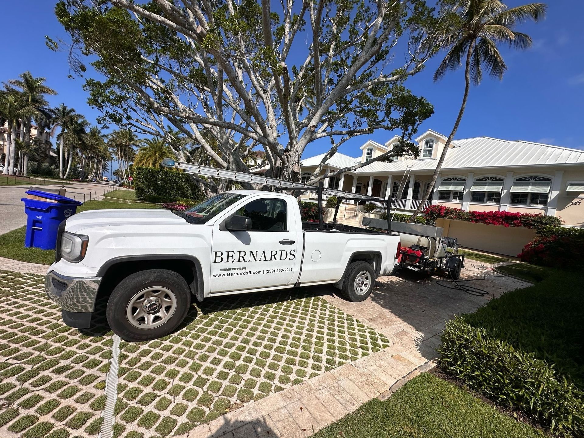 White work truck parked on a grassy paver driveway beside a white building and palm tree under a blue sky