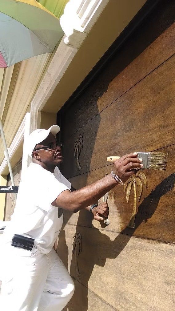Man painting a wooden wall with a brush, wearing white clothes and cap outdoors.