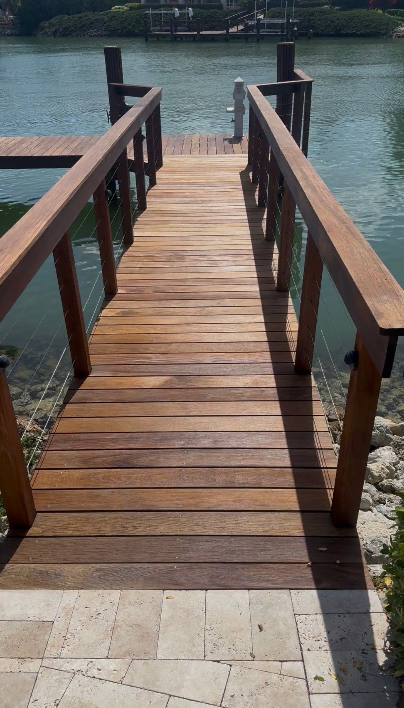 Wooden dock with railings leading out over calm water from a stone landing