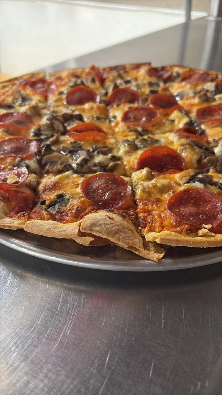 A pizza with pepperoni , mushrooms and cheese is on a pan on a table.