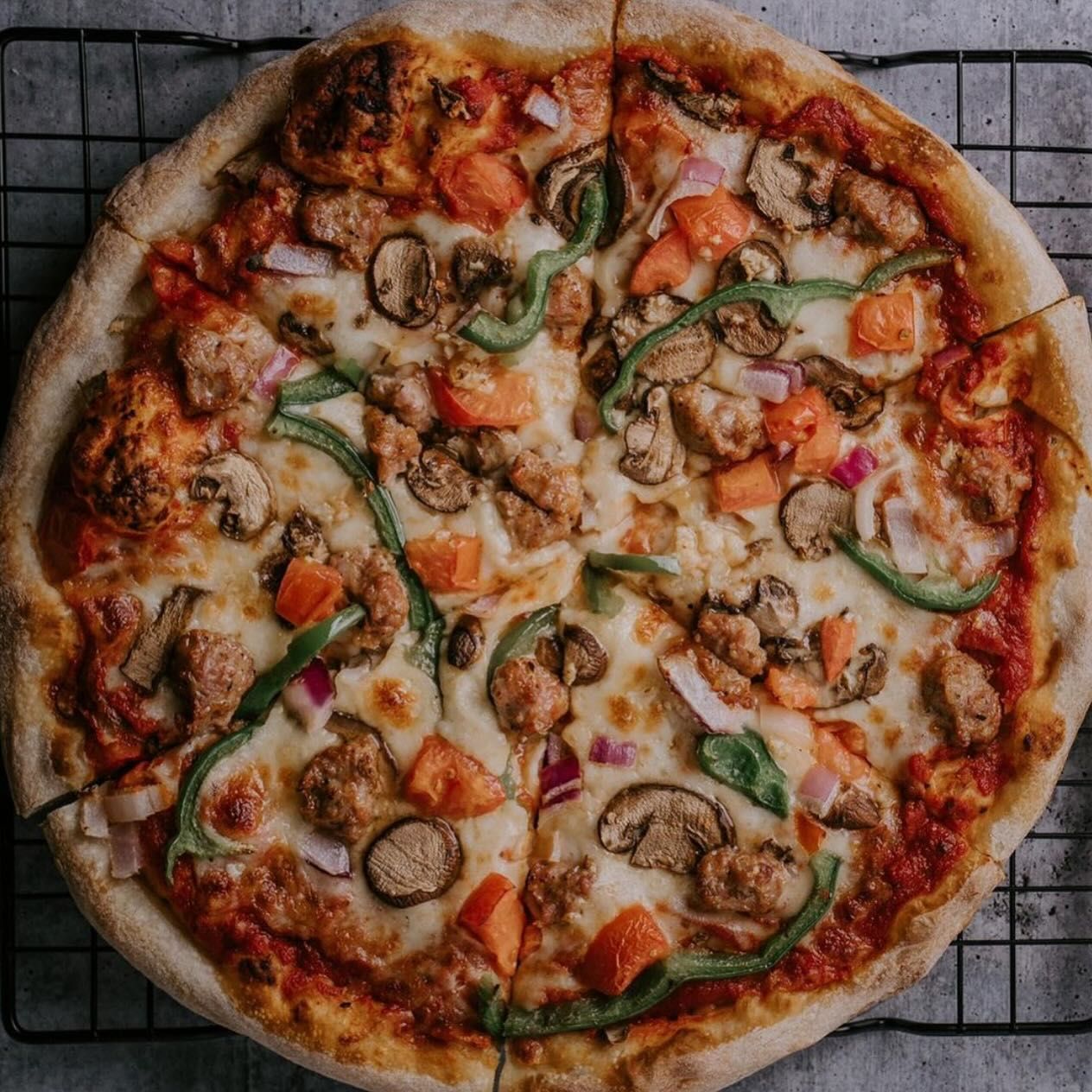 A pizza with a lot of toppings on it is sitting on a cooling rack.