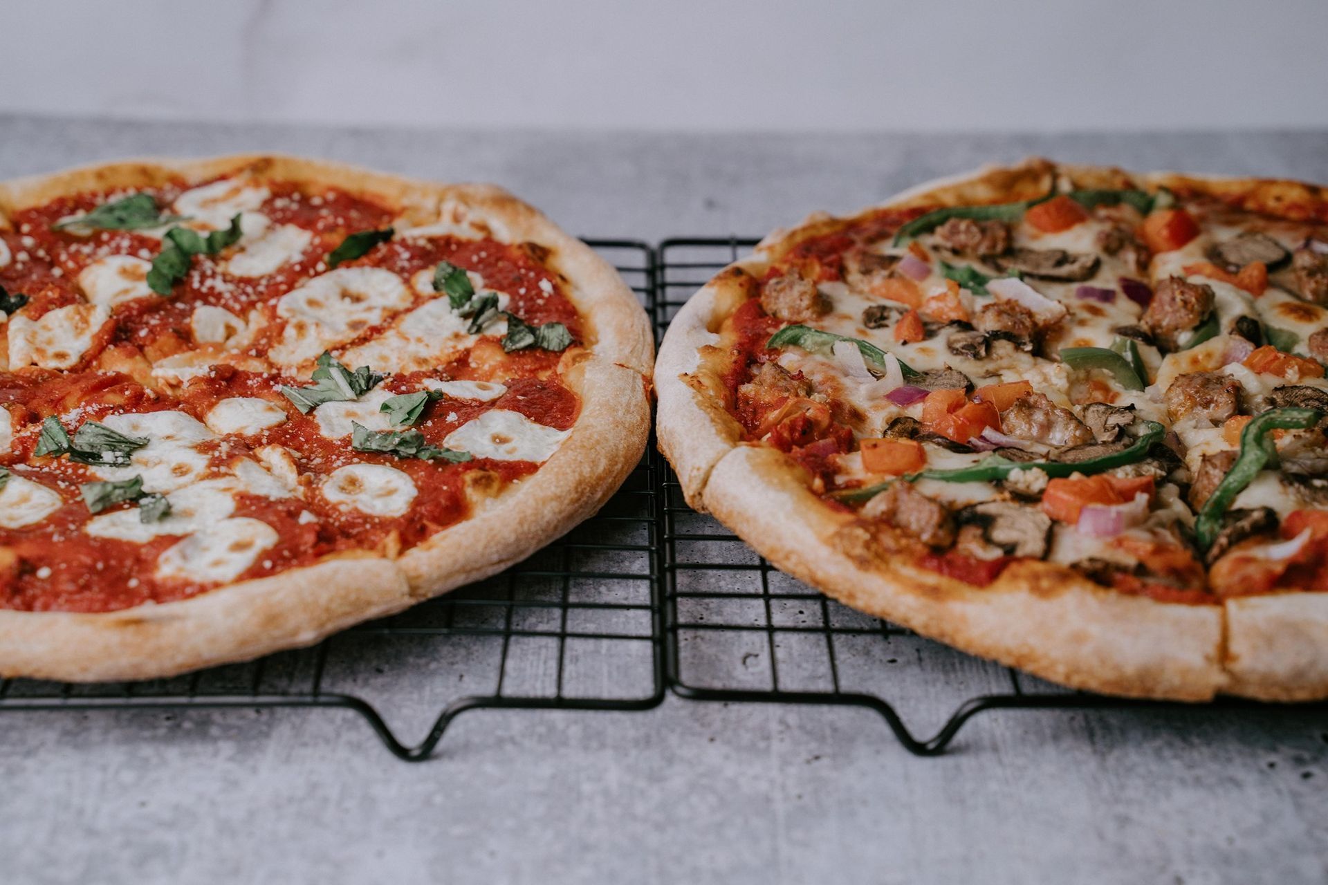 Two pizzas are sitting on a cooling rack on a table.
