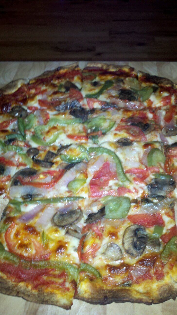 A pizza with tomatoes , peppers , mushrooms and cheese is sitting on a wooden table.