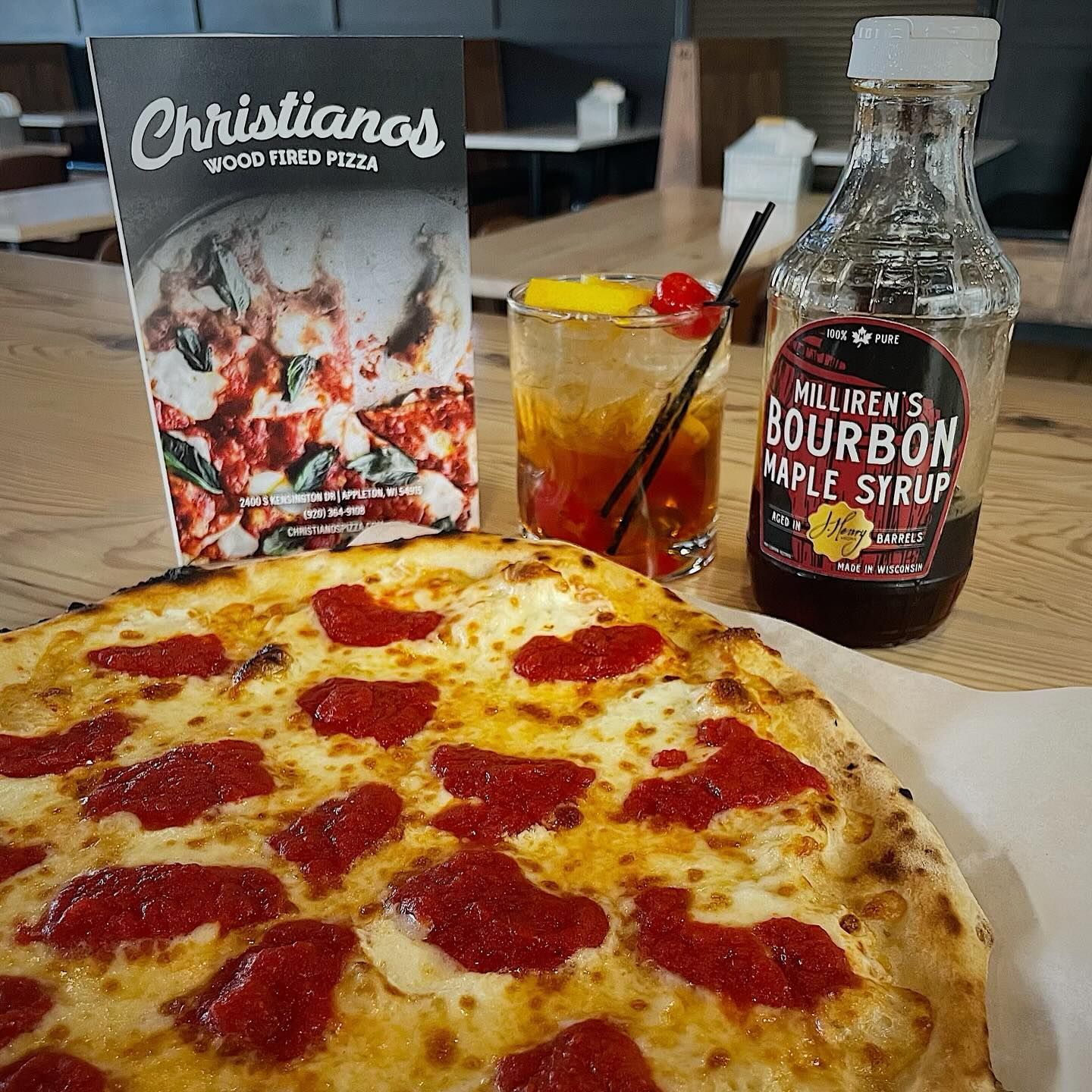 A pepperoni pizza next to a bottle of bourbon maple syrup