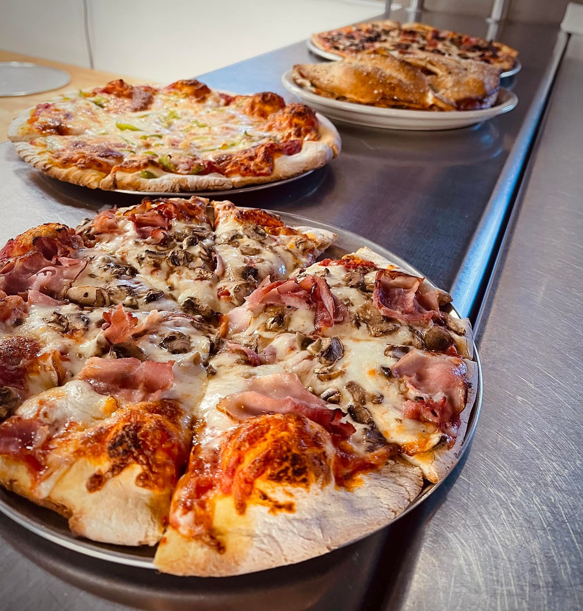 Three pizzas are sitting on a stainless steel counter top