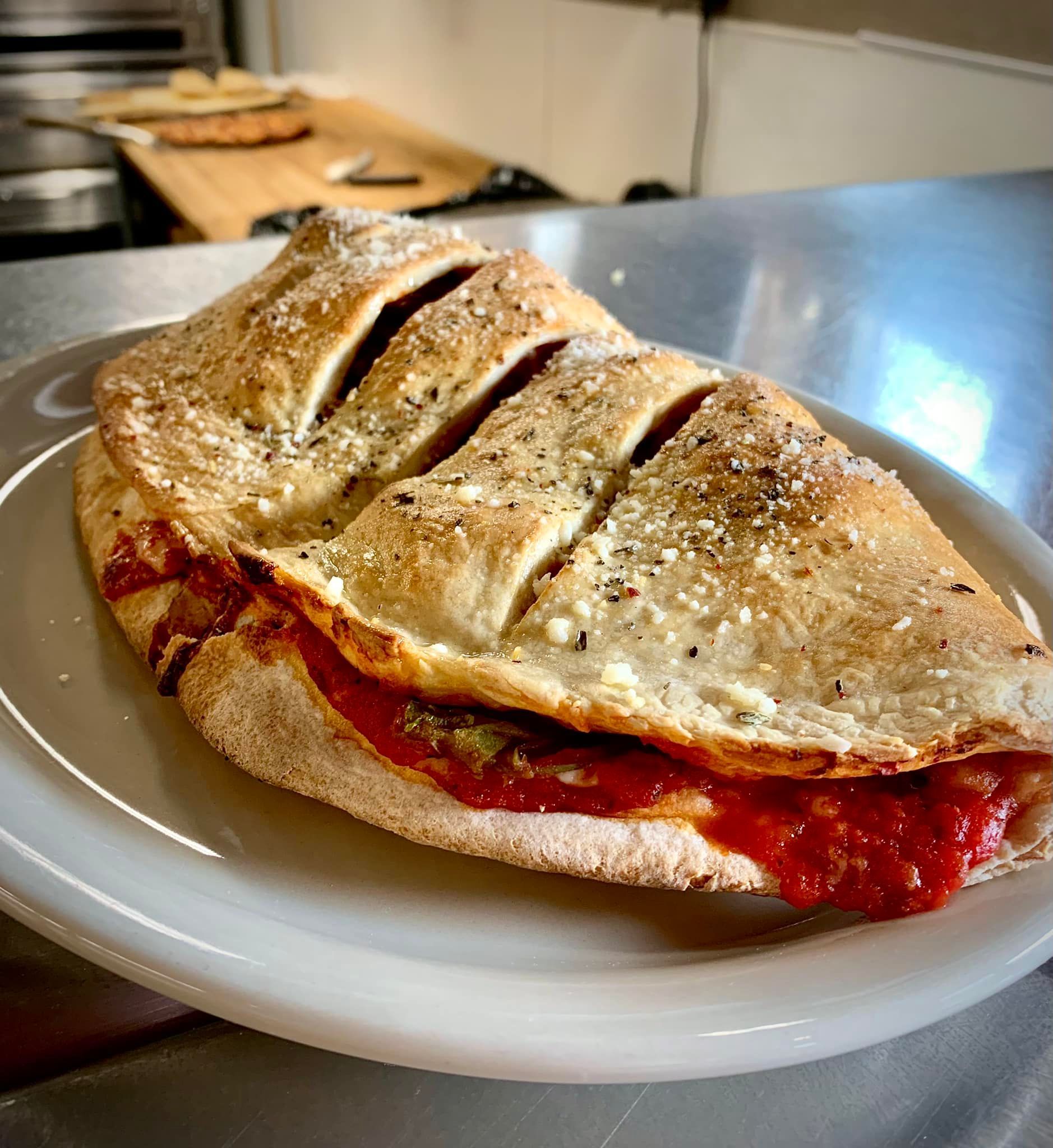 A pizza sandwich is on a white plate on a table.