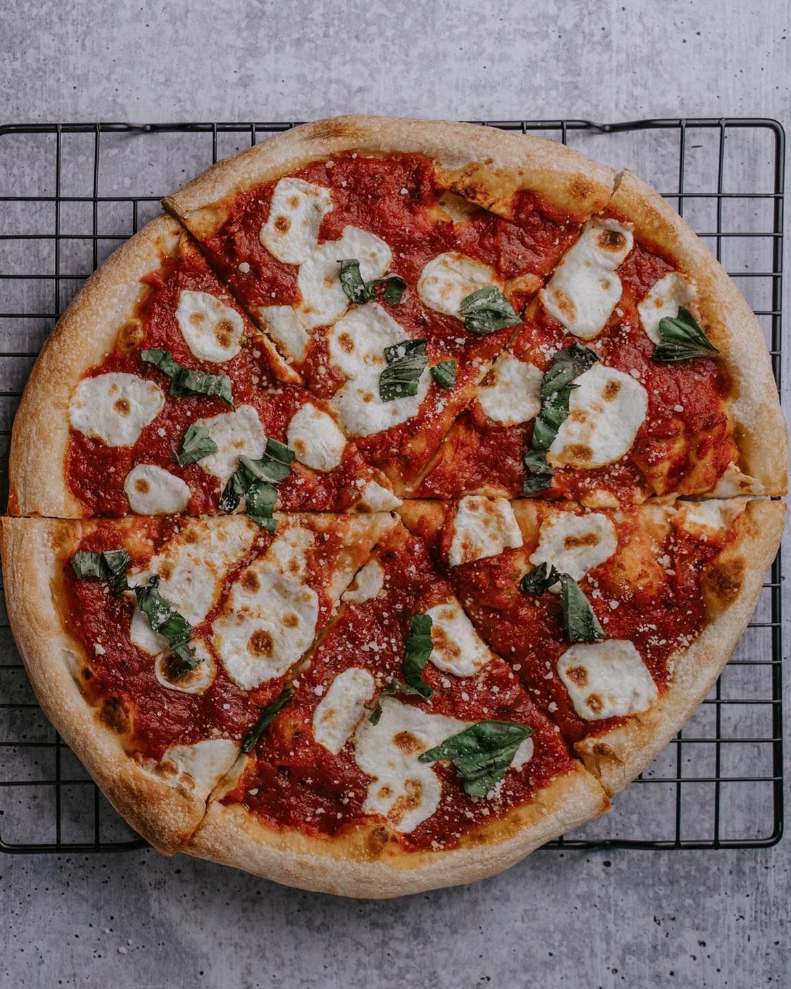 A pizza with tomato sauce and cheese is sitting on a cooling rack.