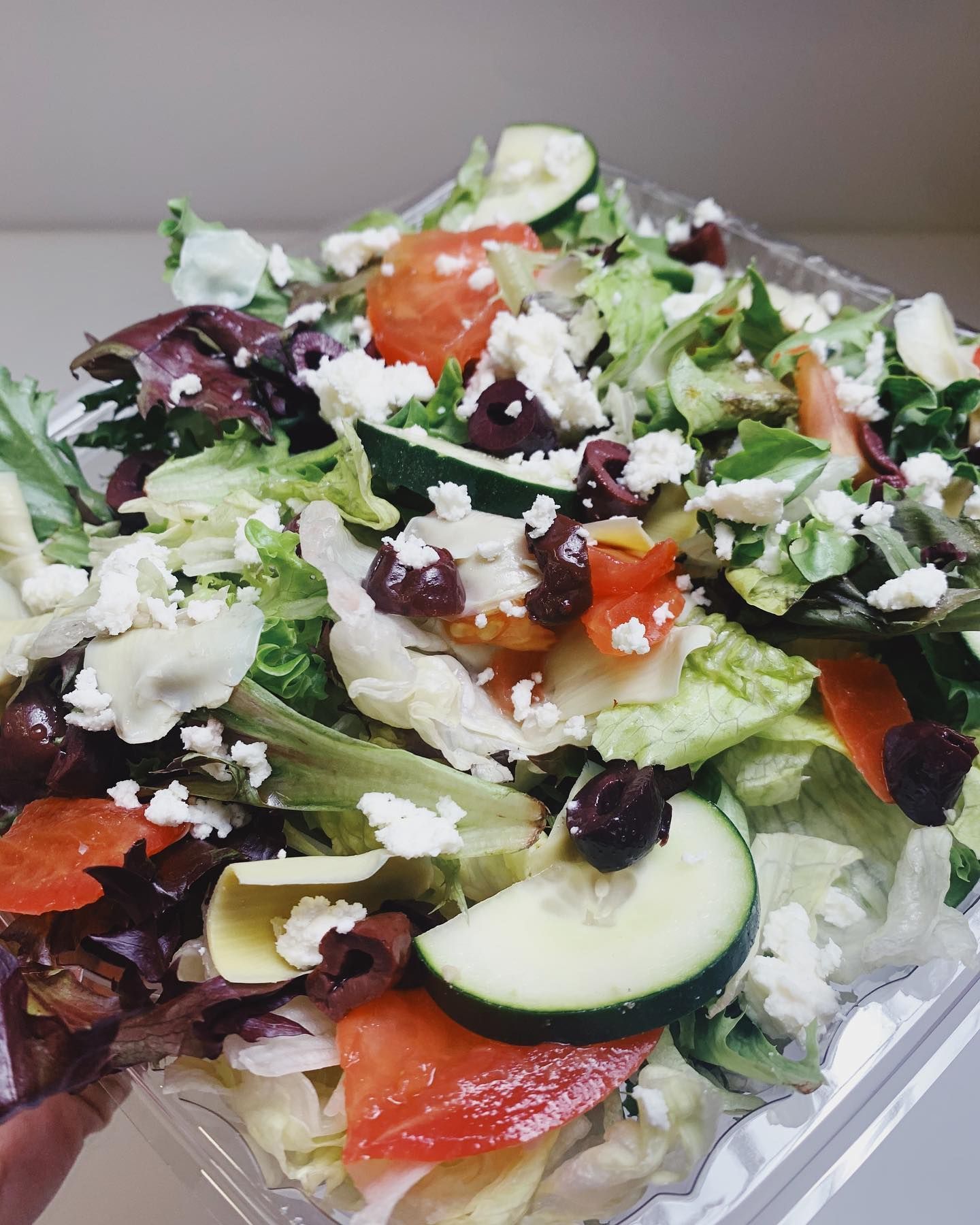 A person is holding a salad in a plastic container