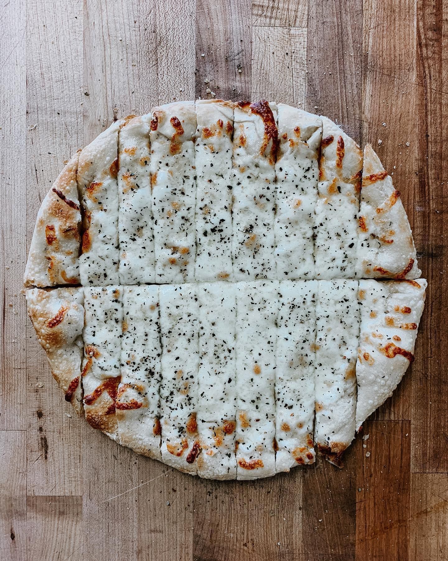 A pizza with cheese sticks on it is sitting on a wooden table.
